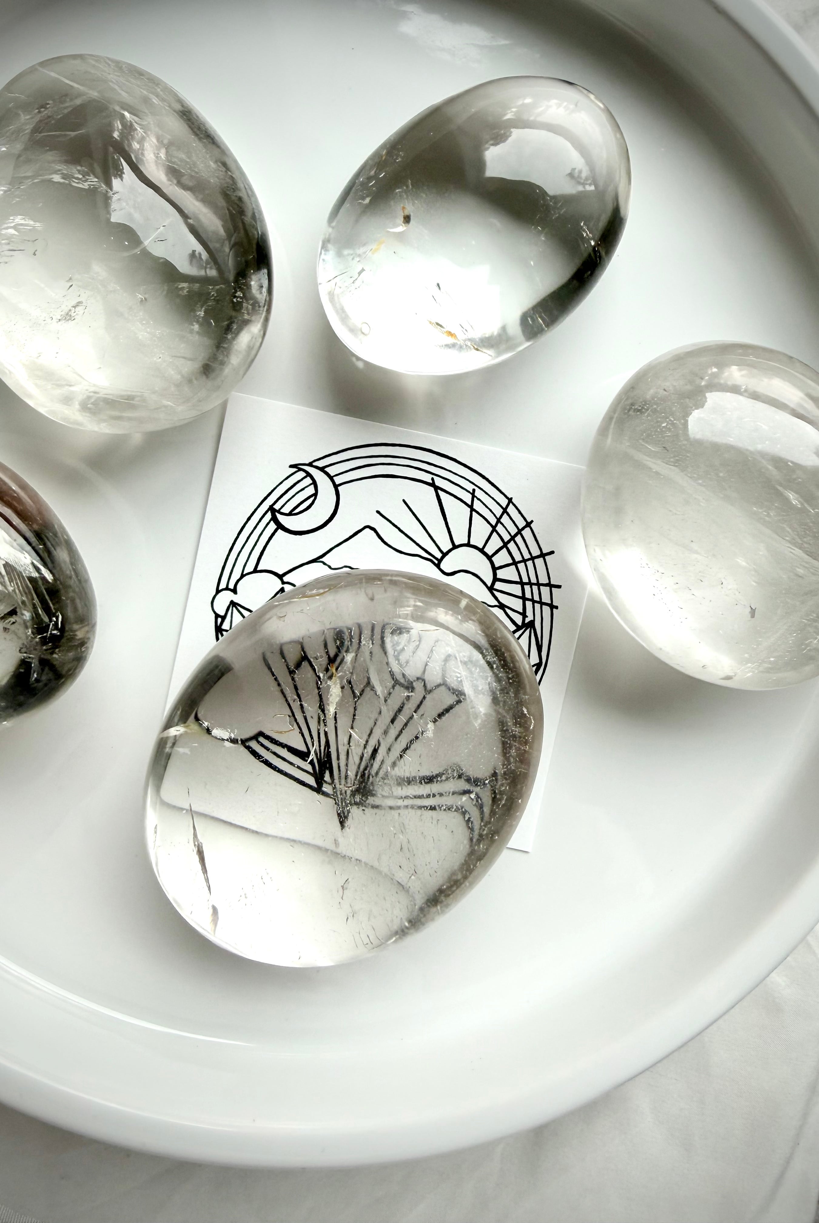 clear quartz palm stones on white tray with brand card beneath stone showing high clarity and natural inclusions