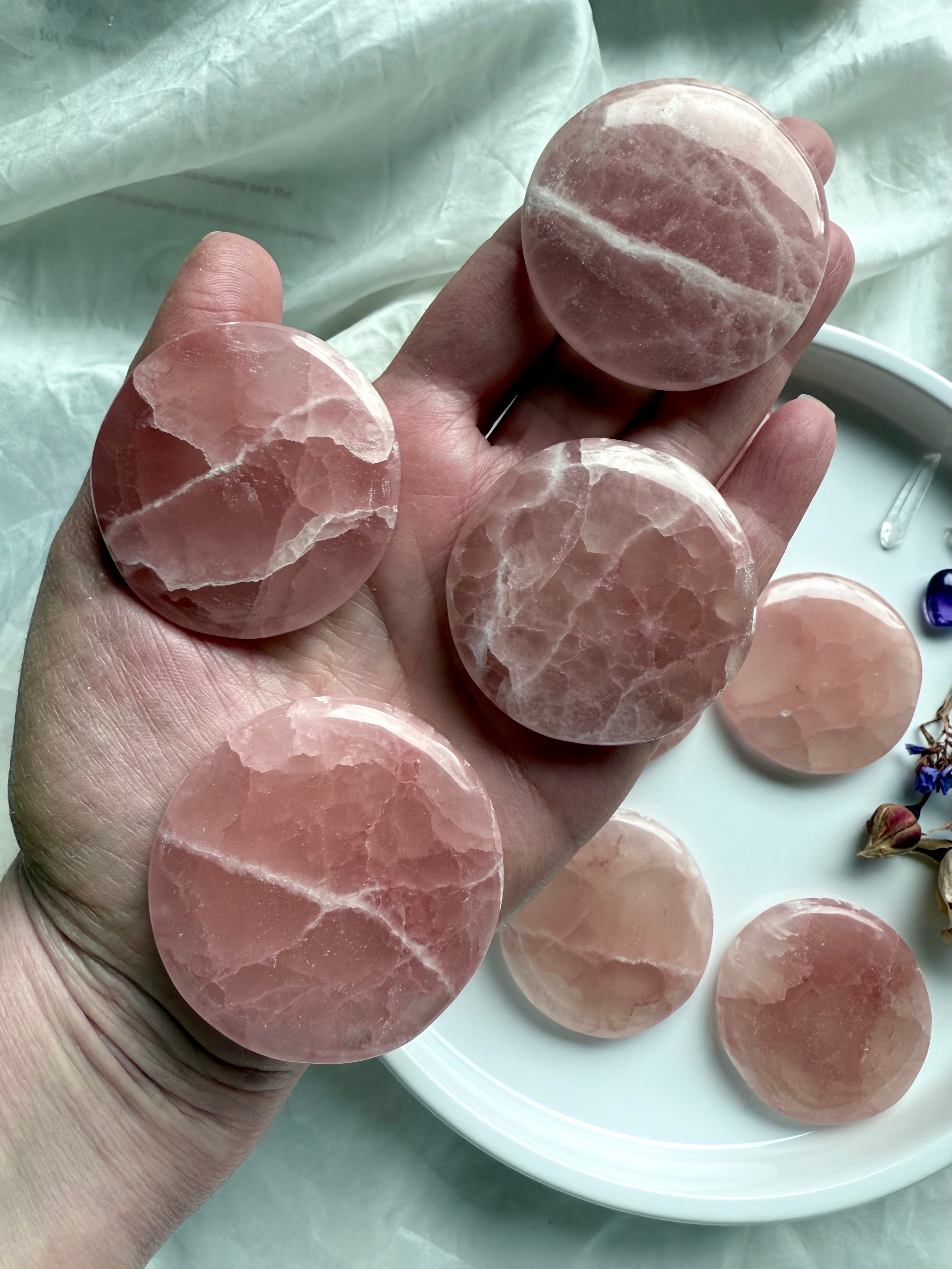 Hand holding four Rose Calcite discs, showing size and natural variation in color and pattern