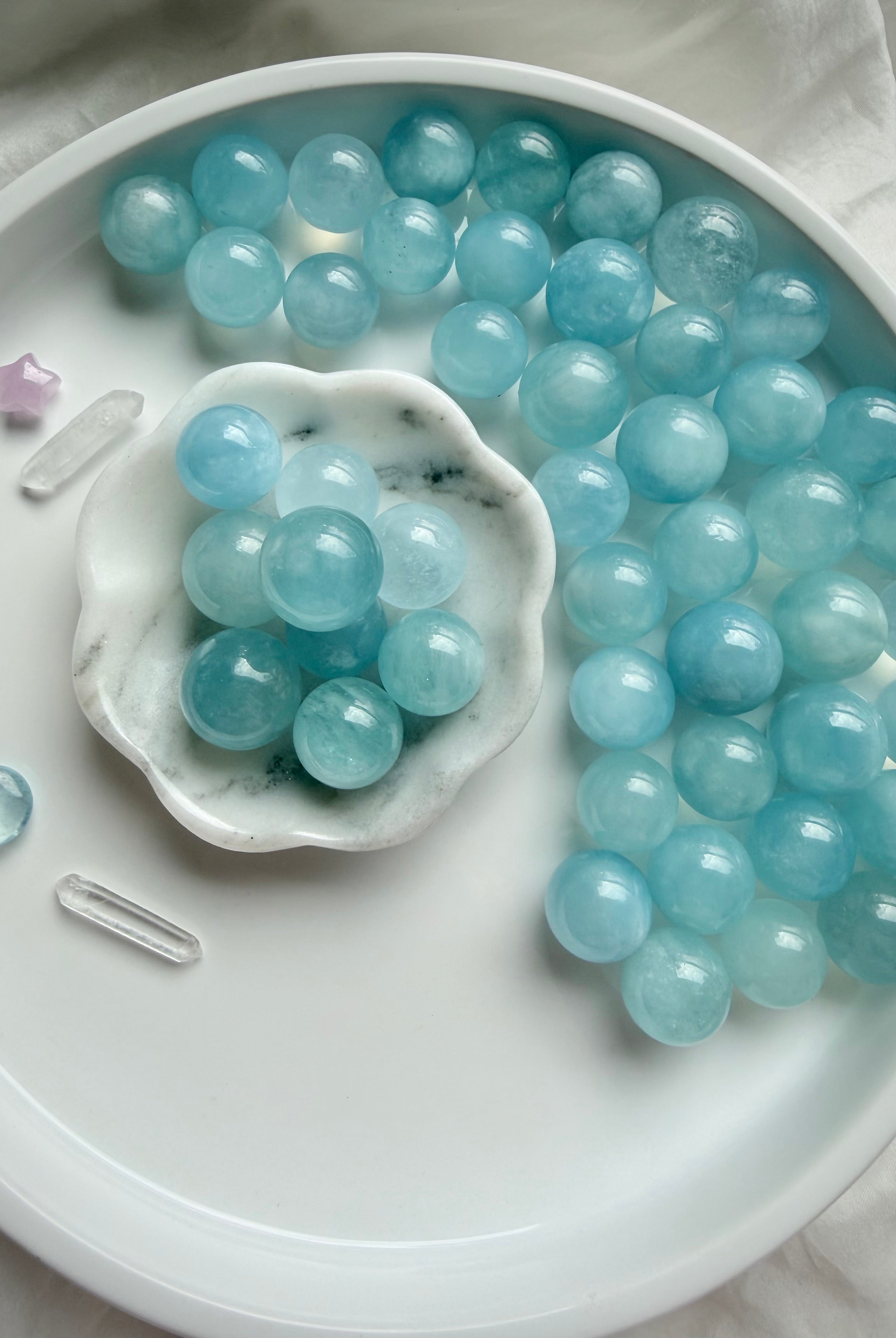 Aquamarine mini blue crystal balls styled on marble dish – soothing March birthstone spheres