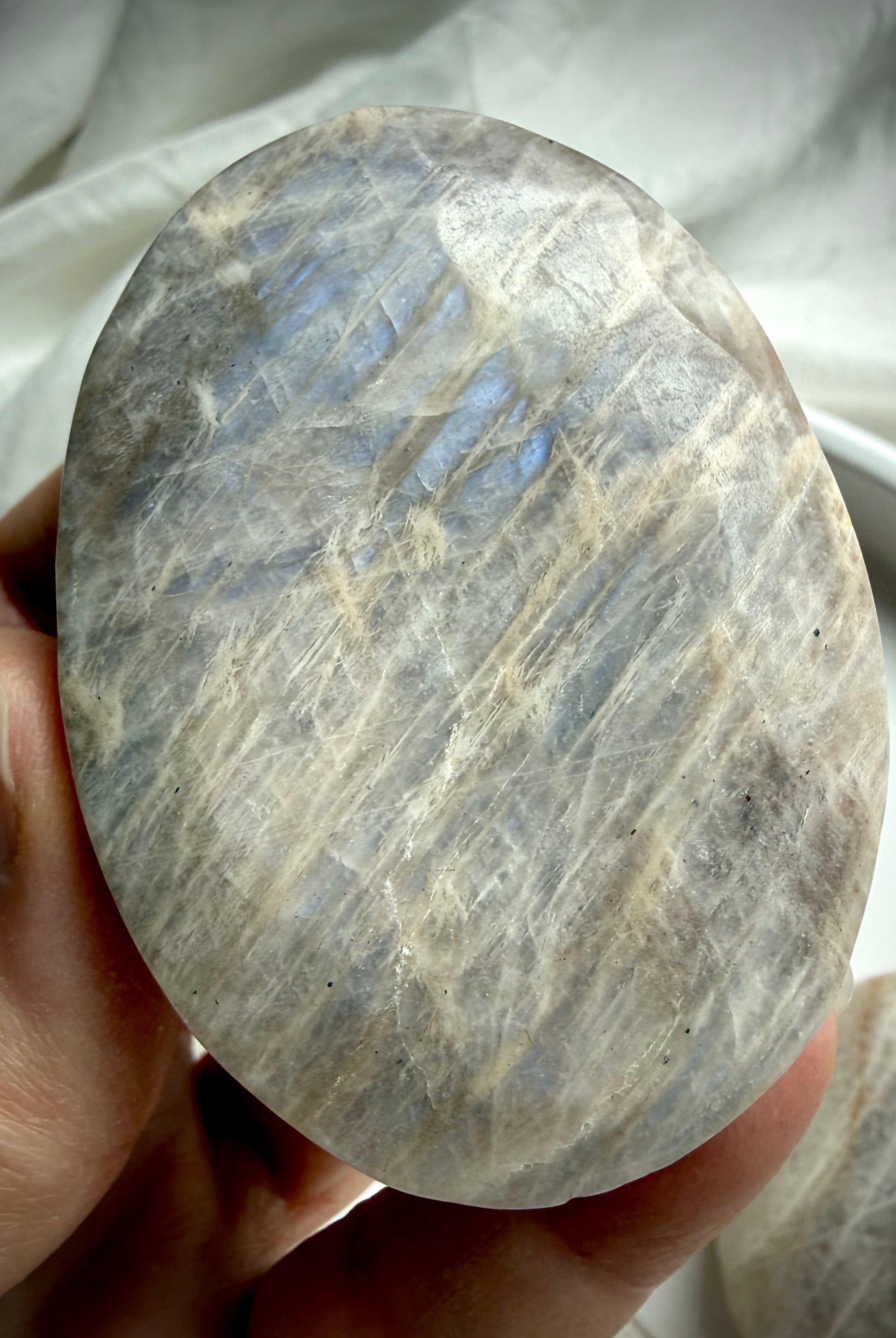 oval belomorite moonstone palm stone with silky silver flash and natural texture in hand