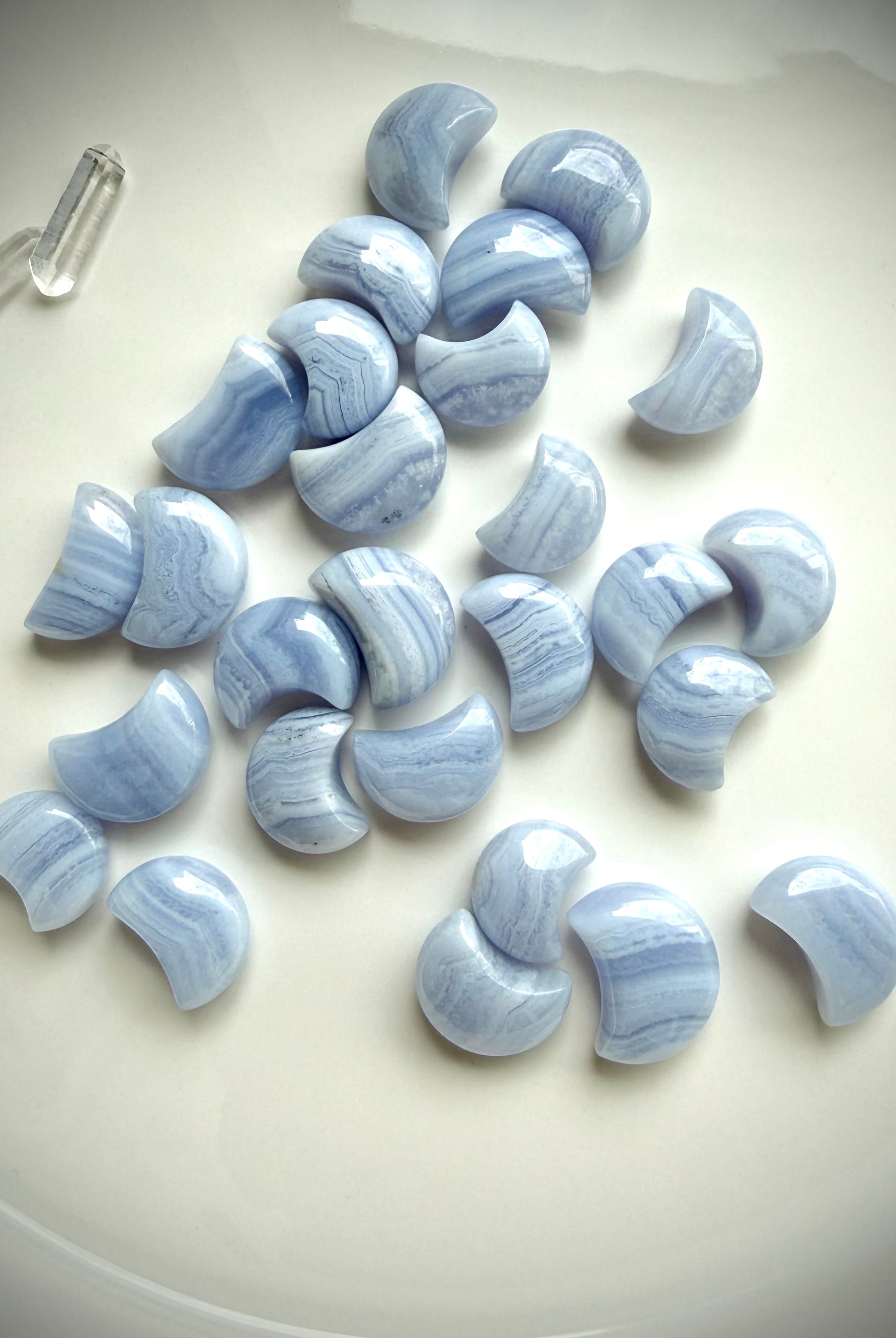 Assorted Blue Lace Agate crescent moon carvings arranged on a white ceramic plate with soft natural light