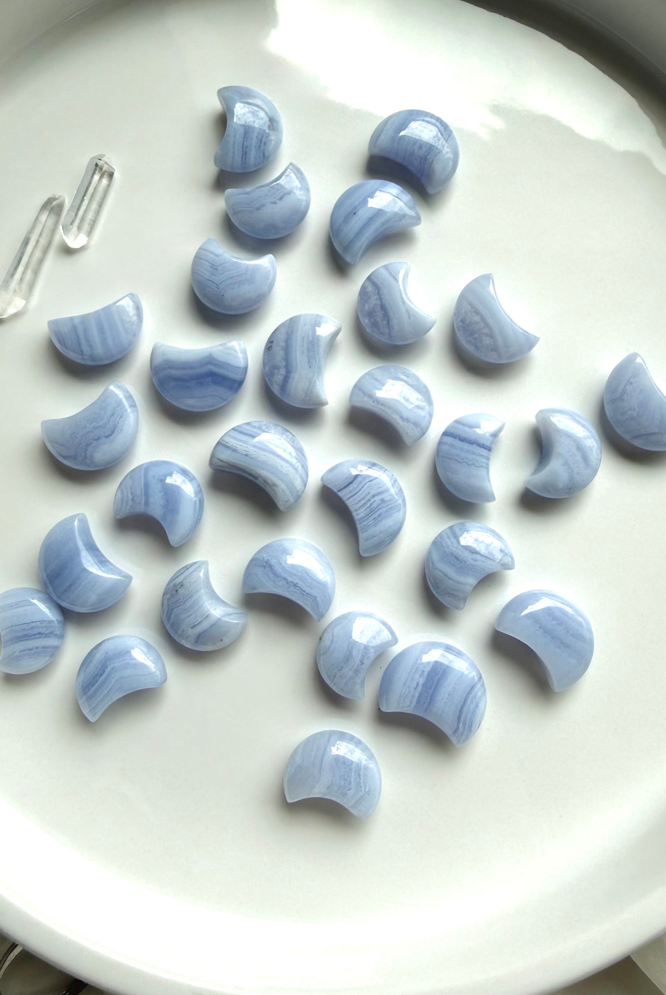Flatlay of Blue Lace Agate crescent moon carvings on a white ceramic plate, calming throat chakra crystals