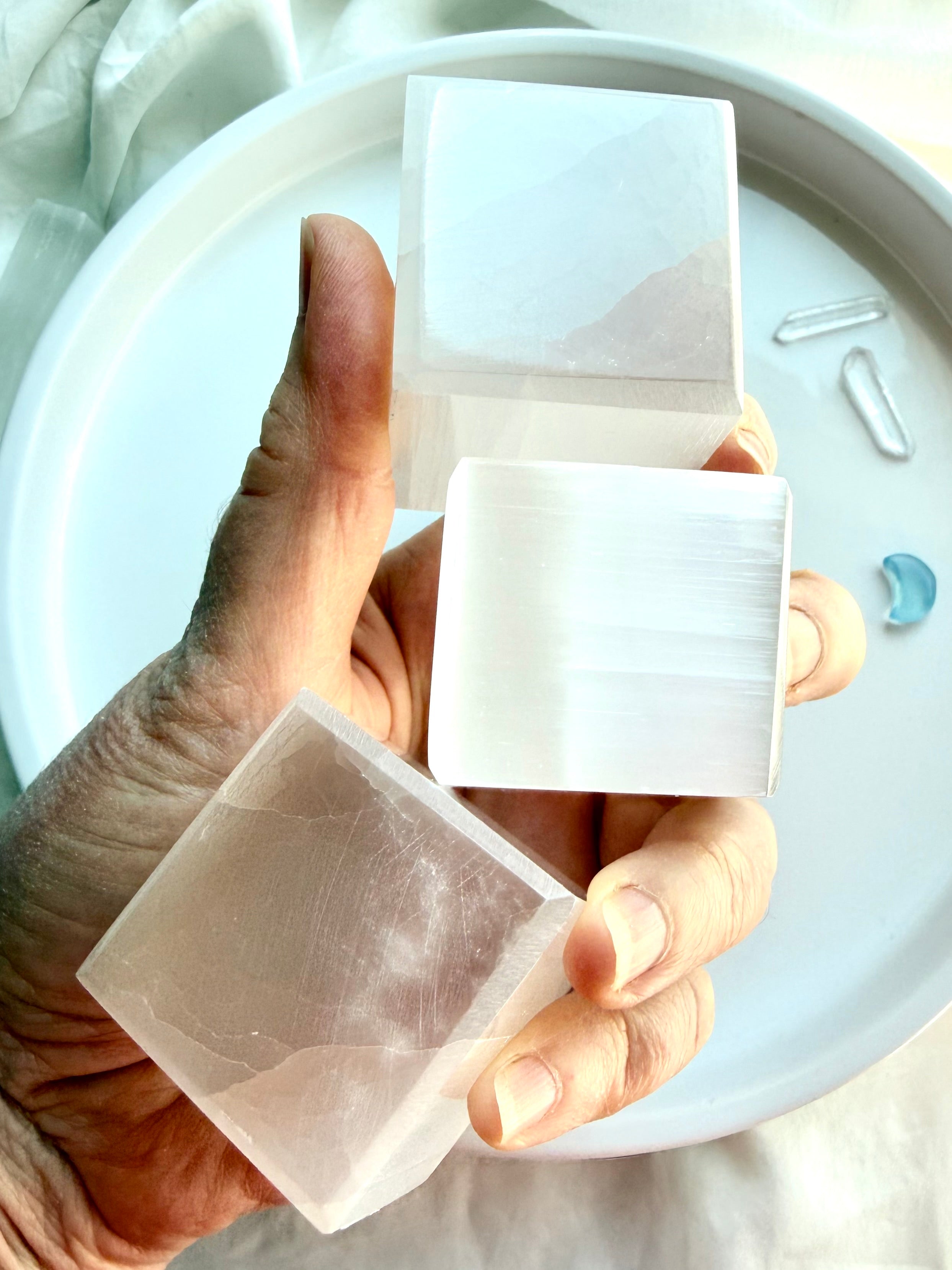 Selenite crystal cube held in bright sunlight showing luminous translucent layers and reflective sheen