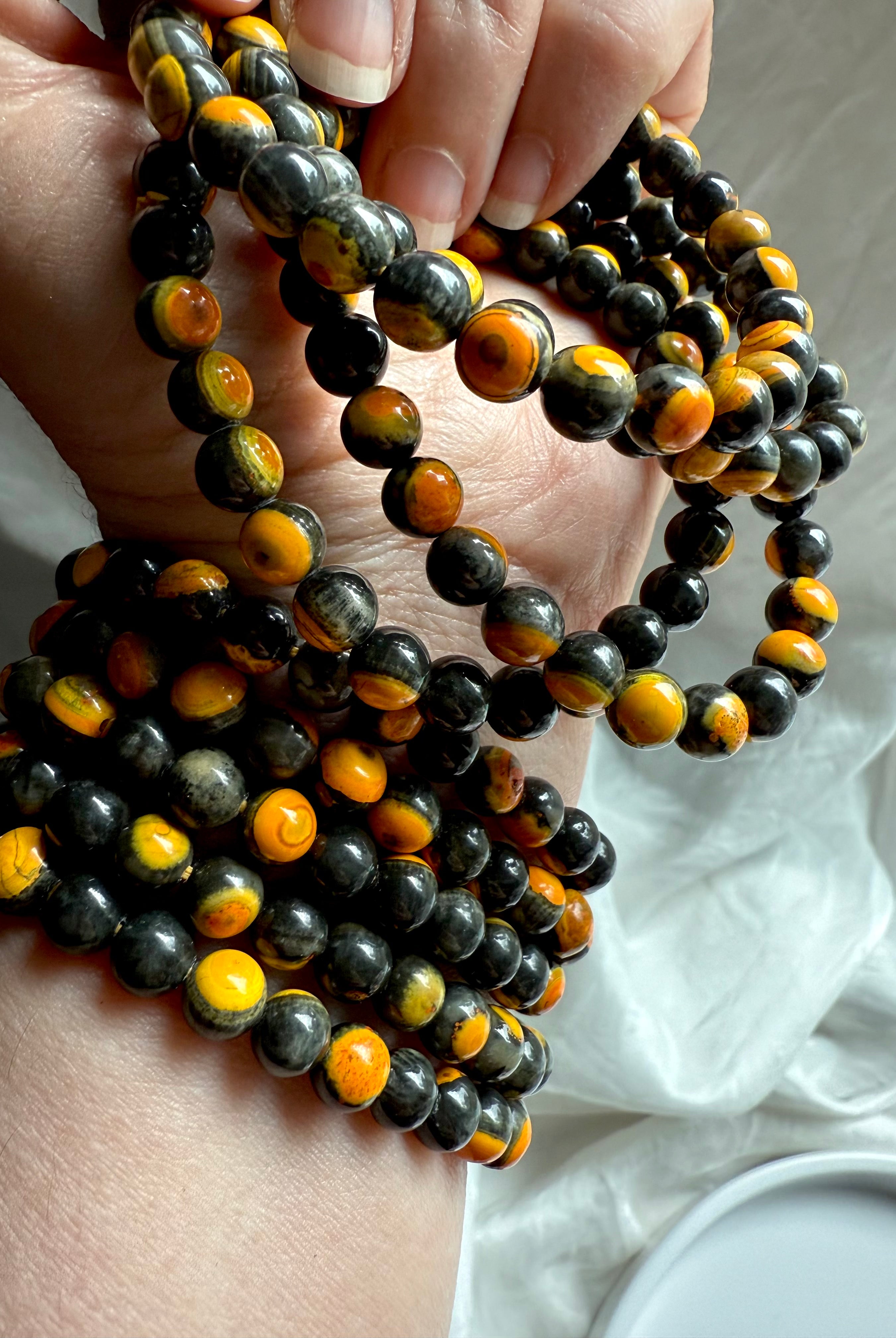Wrist shot of multiple bumblebee jasper bracelets layered with faceted black crystal beads, energizing solar plexus bracelet stack for confidence and grounding