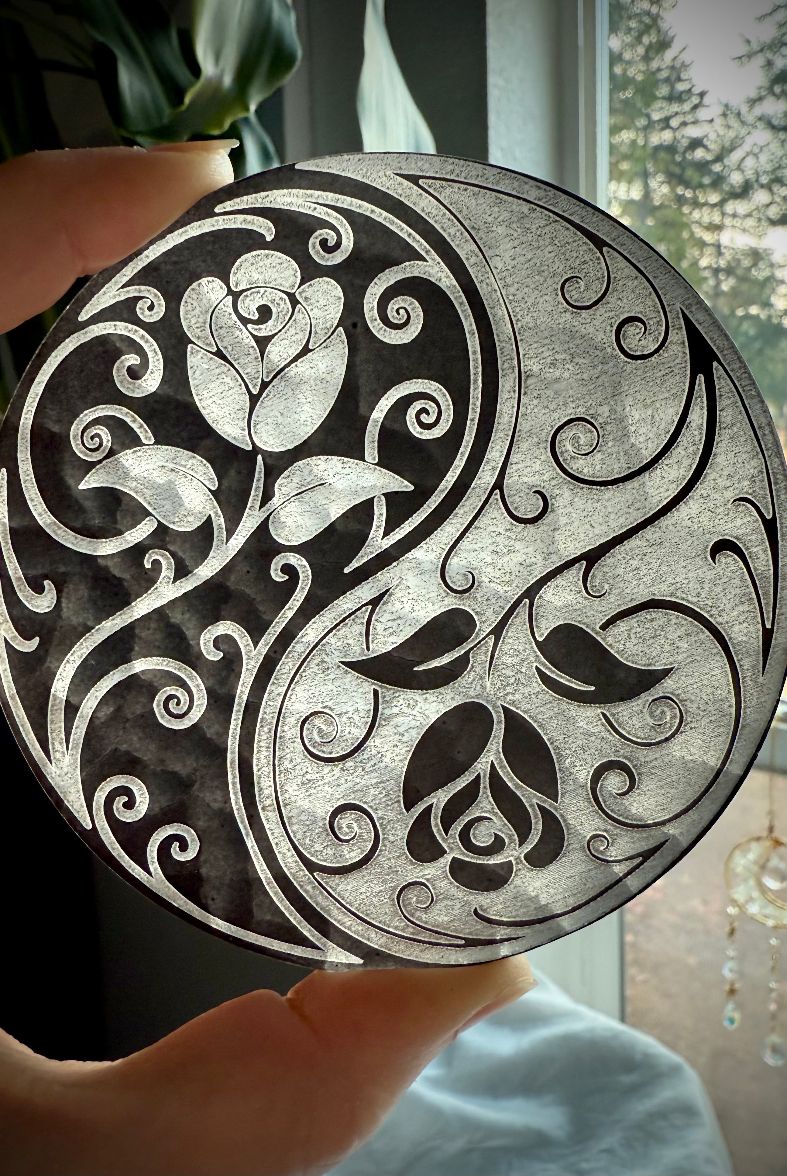Selenite charging plate with yin yang rose design held to light, showing translucence and etched detail