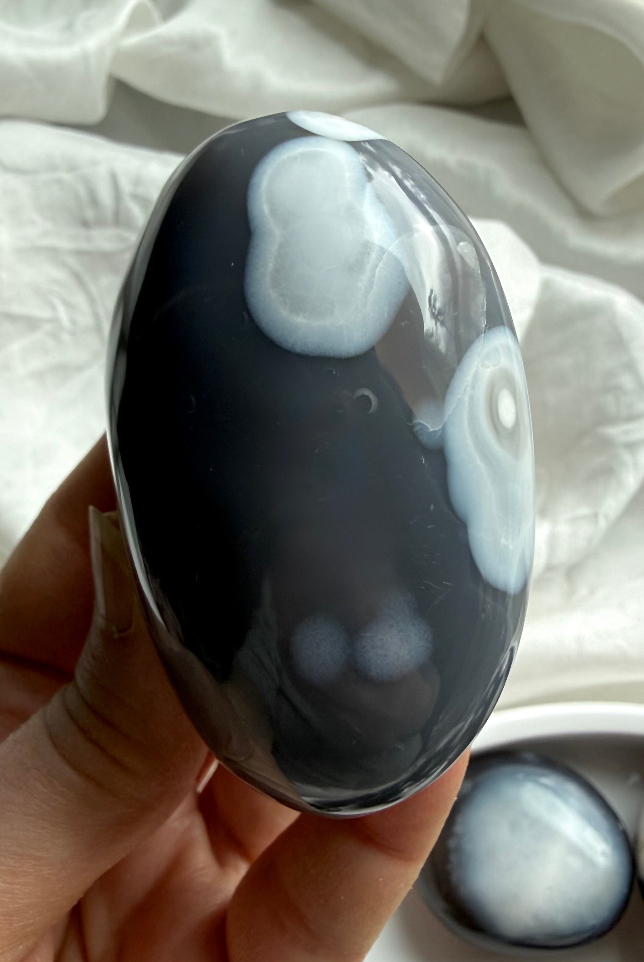 Close-up of Orca Agate palm stone with flowing gray and white agate layers, a grounding crystal for forgiveness and balance