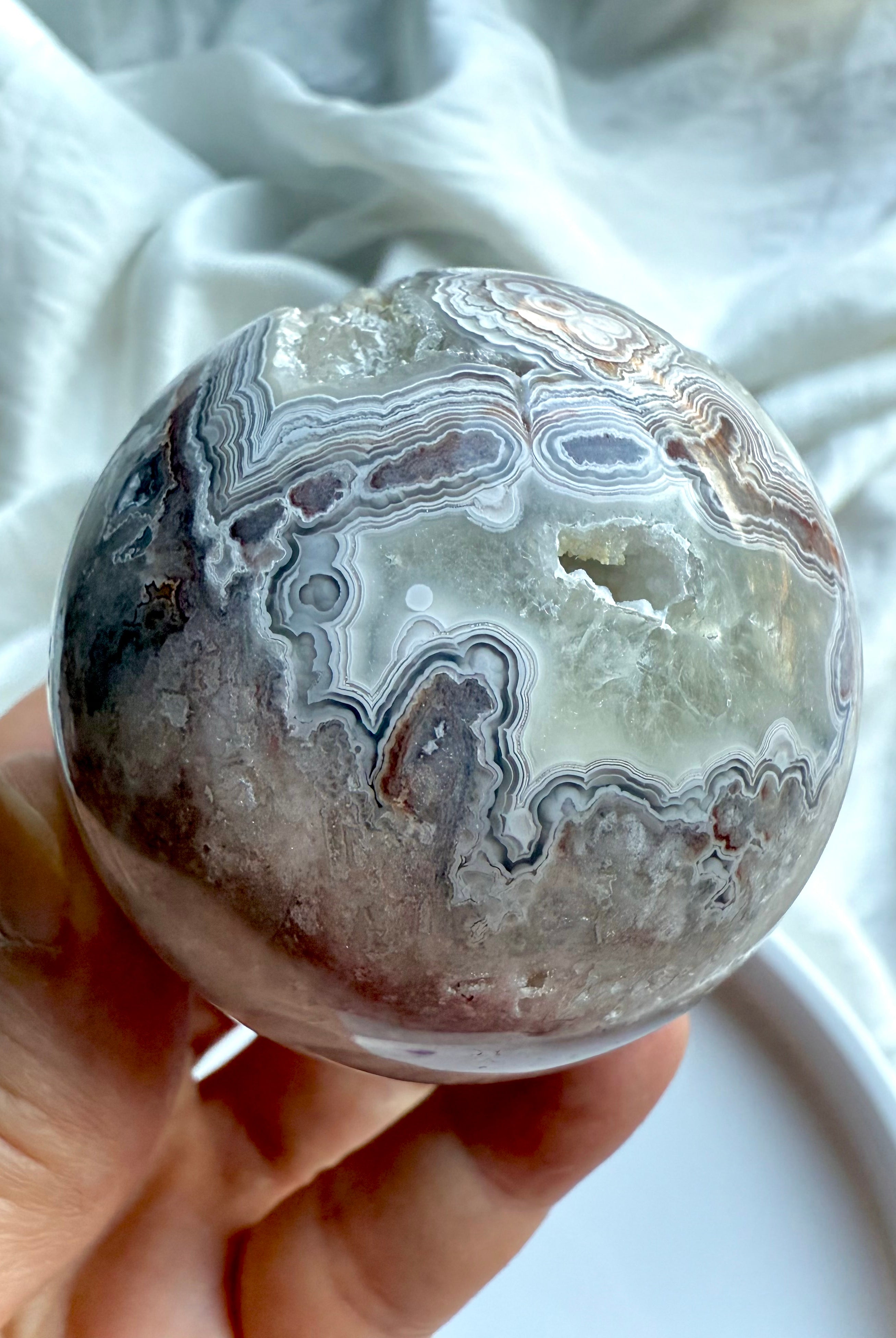 Banded Agate sphere with striking concentric patterns and natural druzy cavity, held in hand on white background