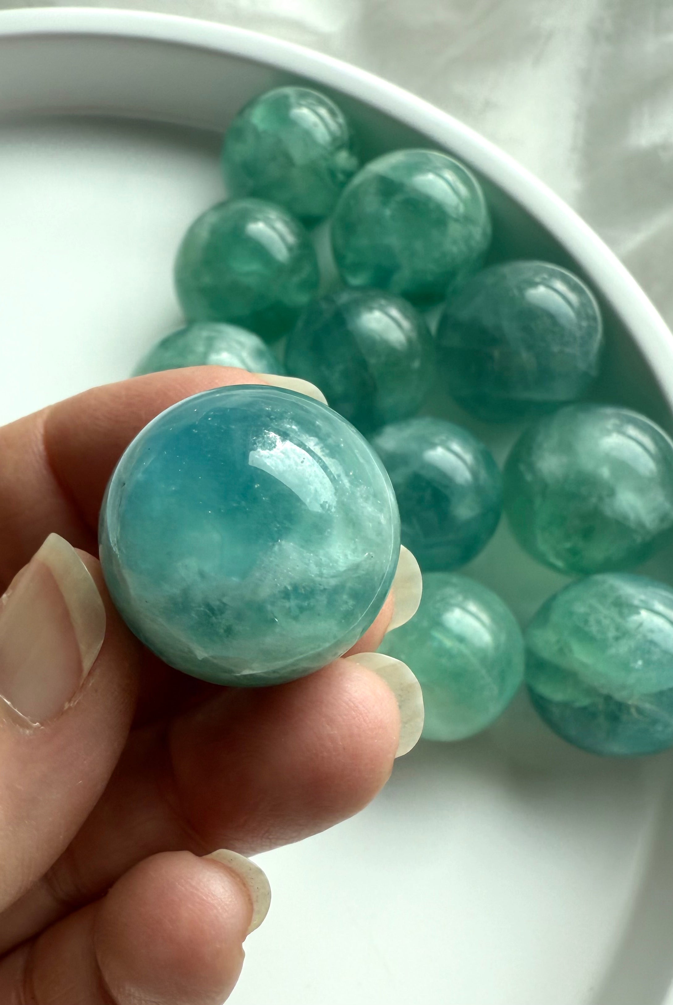 Hand holding a mini aqua teal Fluorite sphere with swirling translucence, rare crystal for calm and spiritual focus.