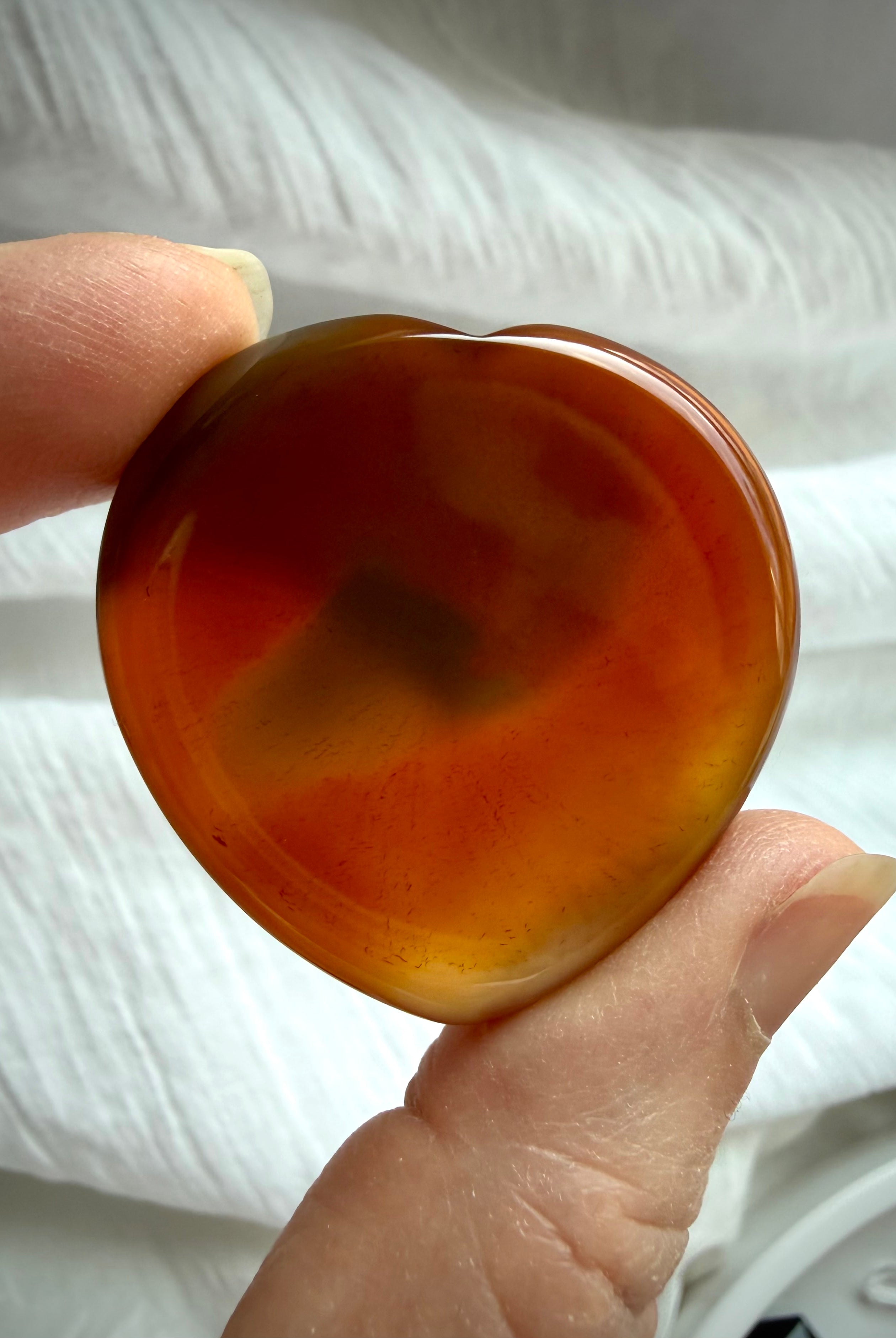 Translucent Carnelian heart worry stone held to light showing warm amber, red and golden natural inclusions