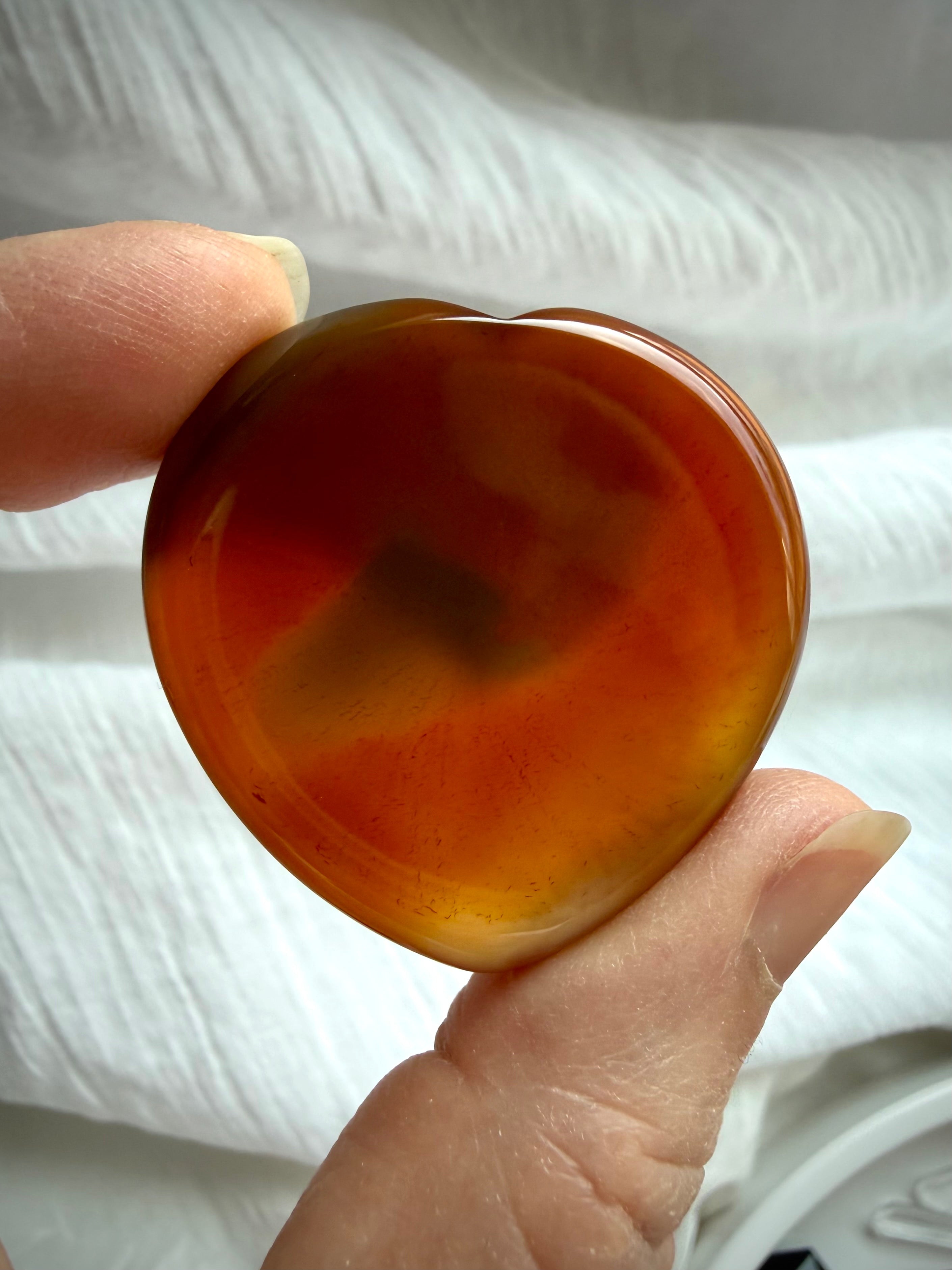 Translucent Carnelian heart worry stone held to light showing warm amber, red and golden natural inclusions