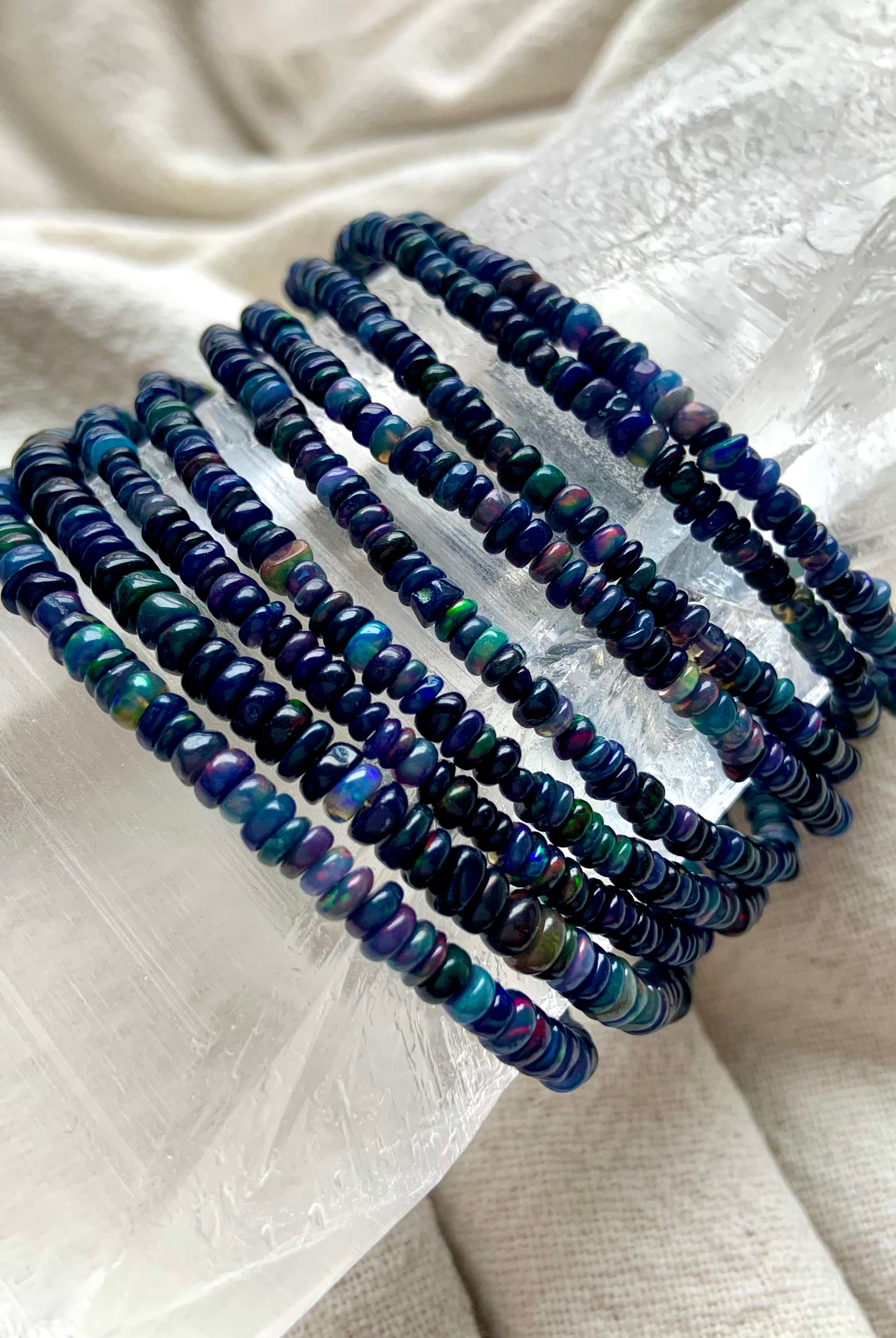 Bracelets draped over a quartz crystal — Genuine Black Opal bead bracelet with rainbow flash — sterling silver October birthstone jewelry gift.