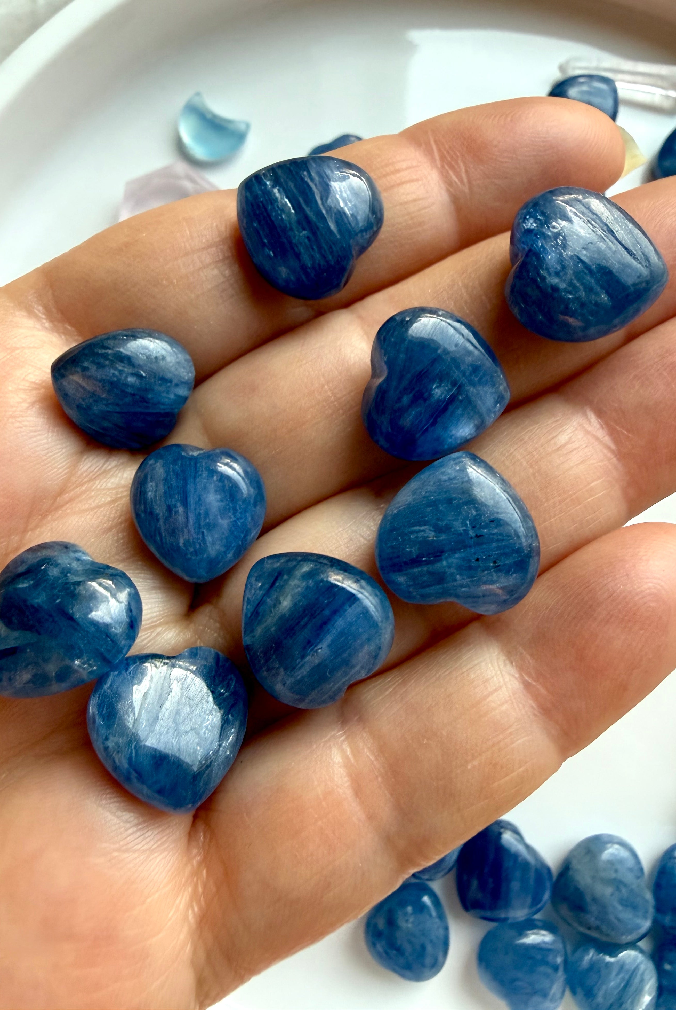 Mini Blue Kyanite heart crystals held in hand showing natural silvery blue shimmer and quartz inclusions, throat chakra healing stones
