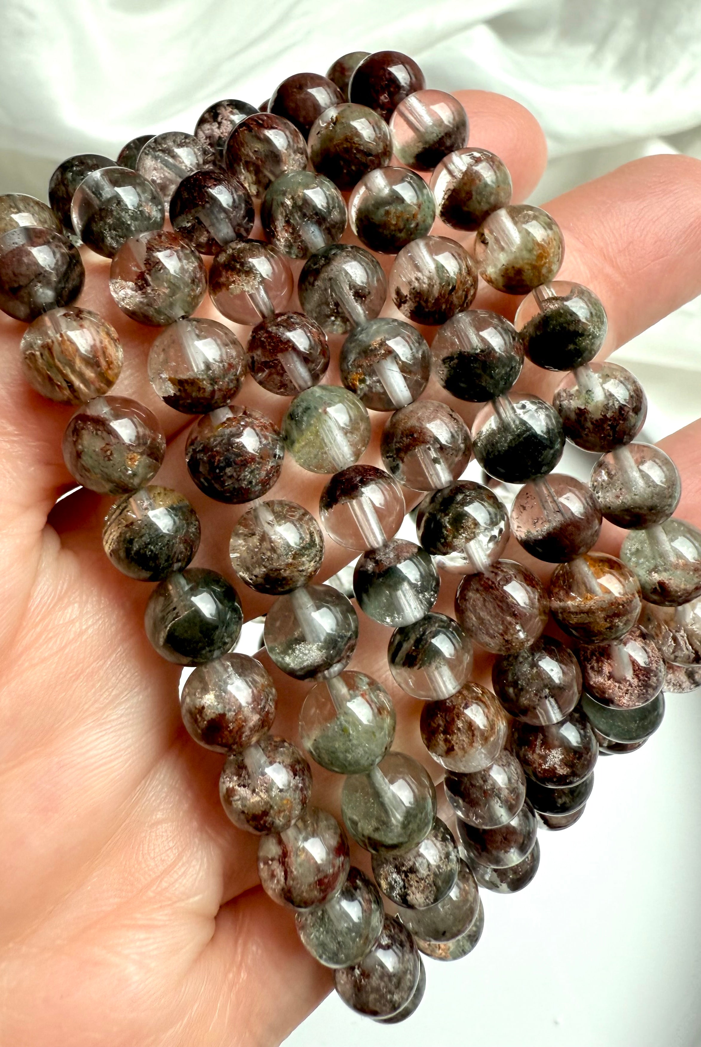 Hand holding Garden Quartz bracelets with scenic mineral formations inside transparent quartz spheres