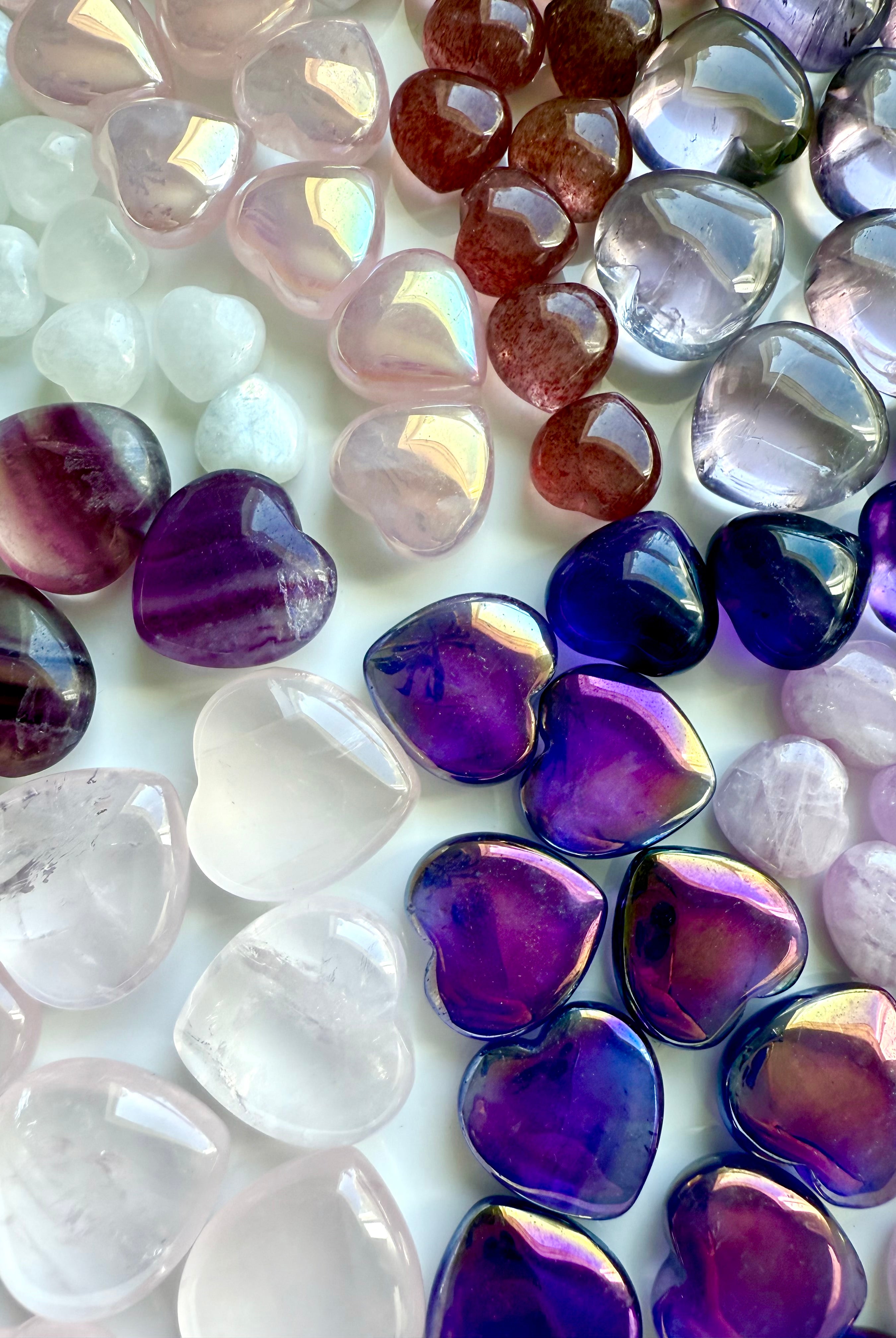 Flat lay of nine types of pink and purple mini crystal hearts, arranged in a pie-slice formation by stone type, premium gemstone carvings.