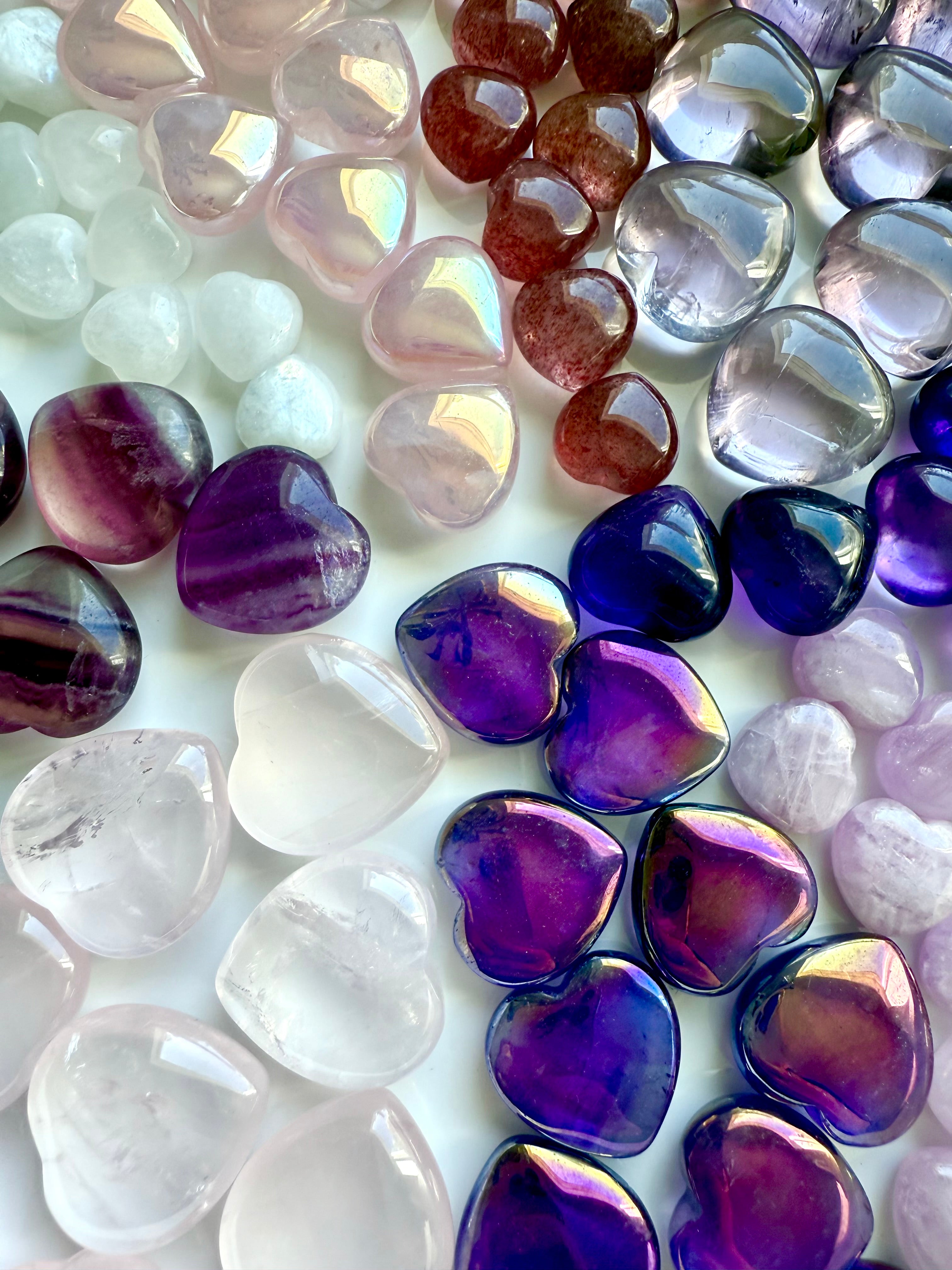 Flat lay of nine types of pink and purple mini crystal hearts, arranged in a pie-slice formation by stone type, premium gemstone carvings.