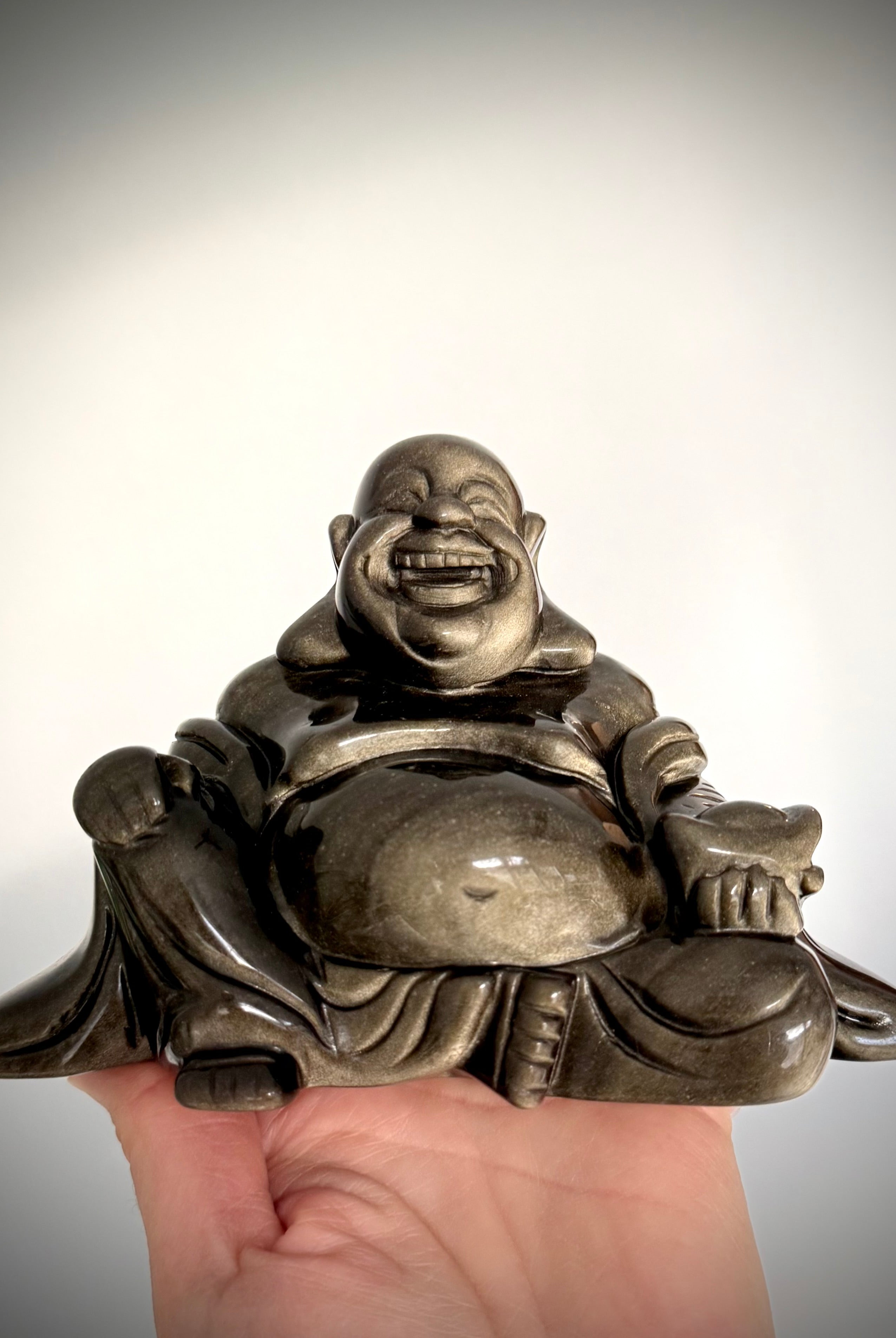 Close-up of laughing Buddha statue carved in Golden Sheen Obsidian, high-vibe crystal for manifestation and protection