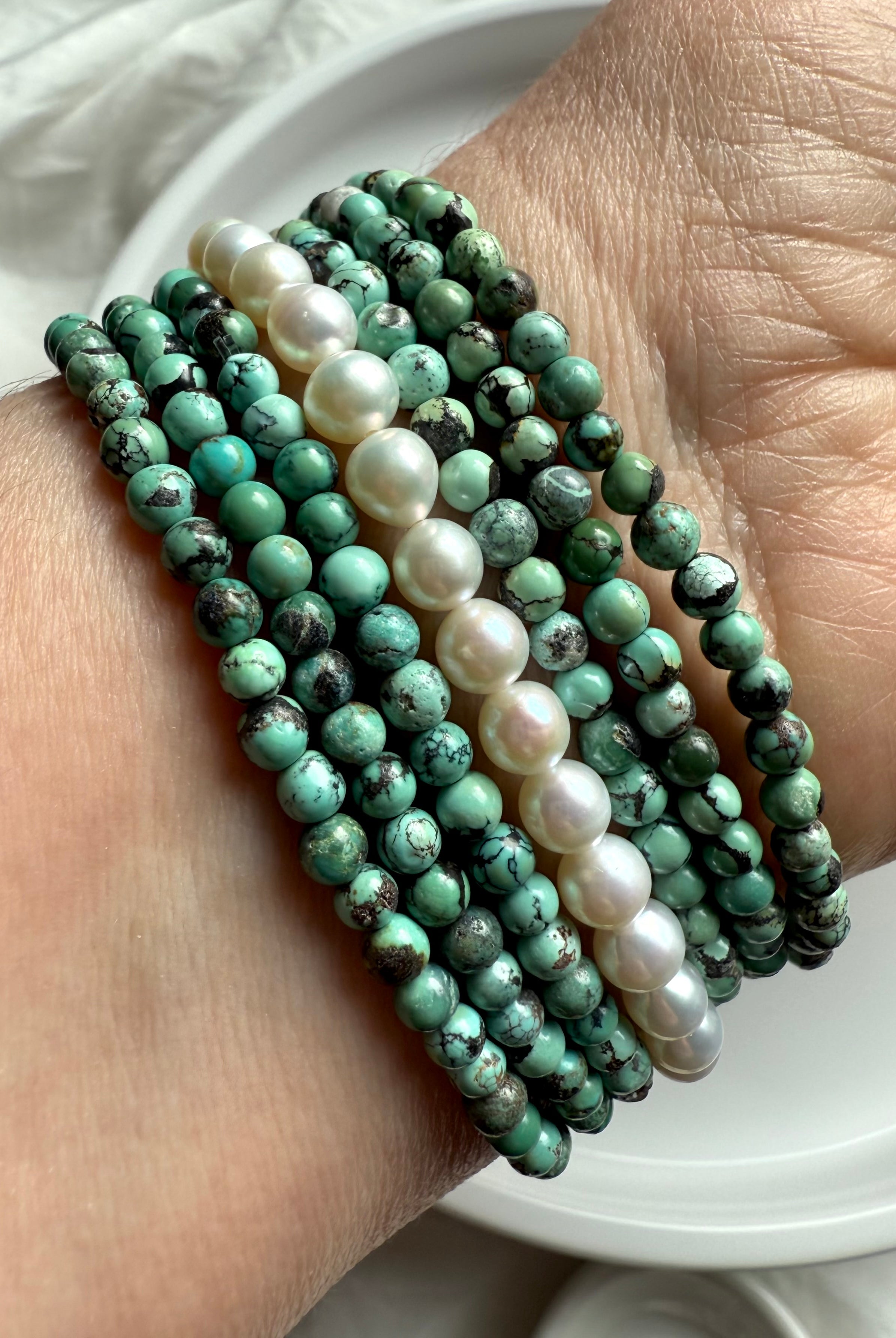 Stacked turquoise and freshwater pearl bead bracelets on wrist with soft natural light