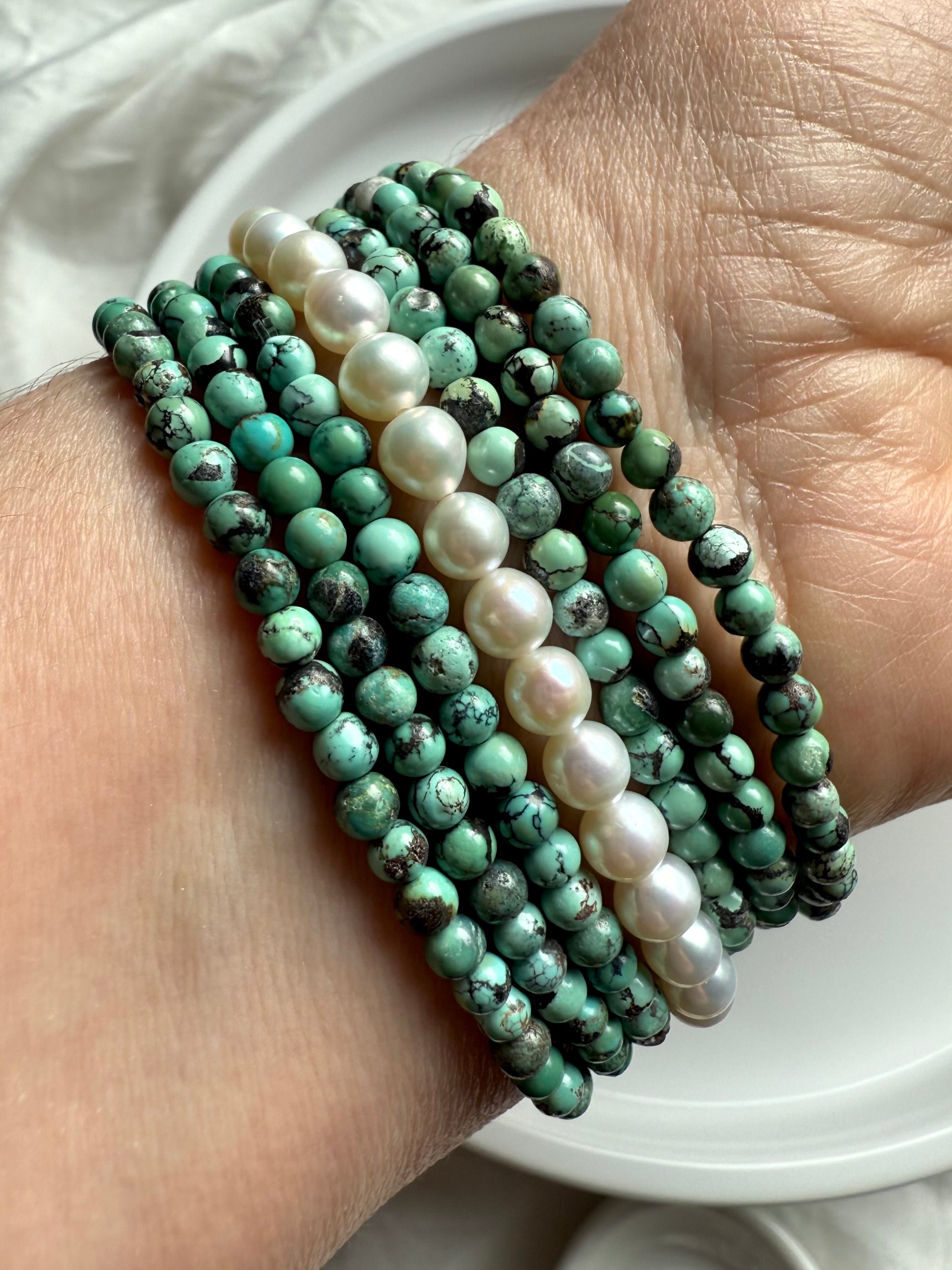 Stacked turquoise and freshwater pearl bead bracelets on wrist with soft natural light
