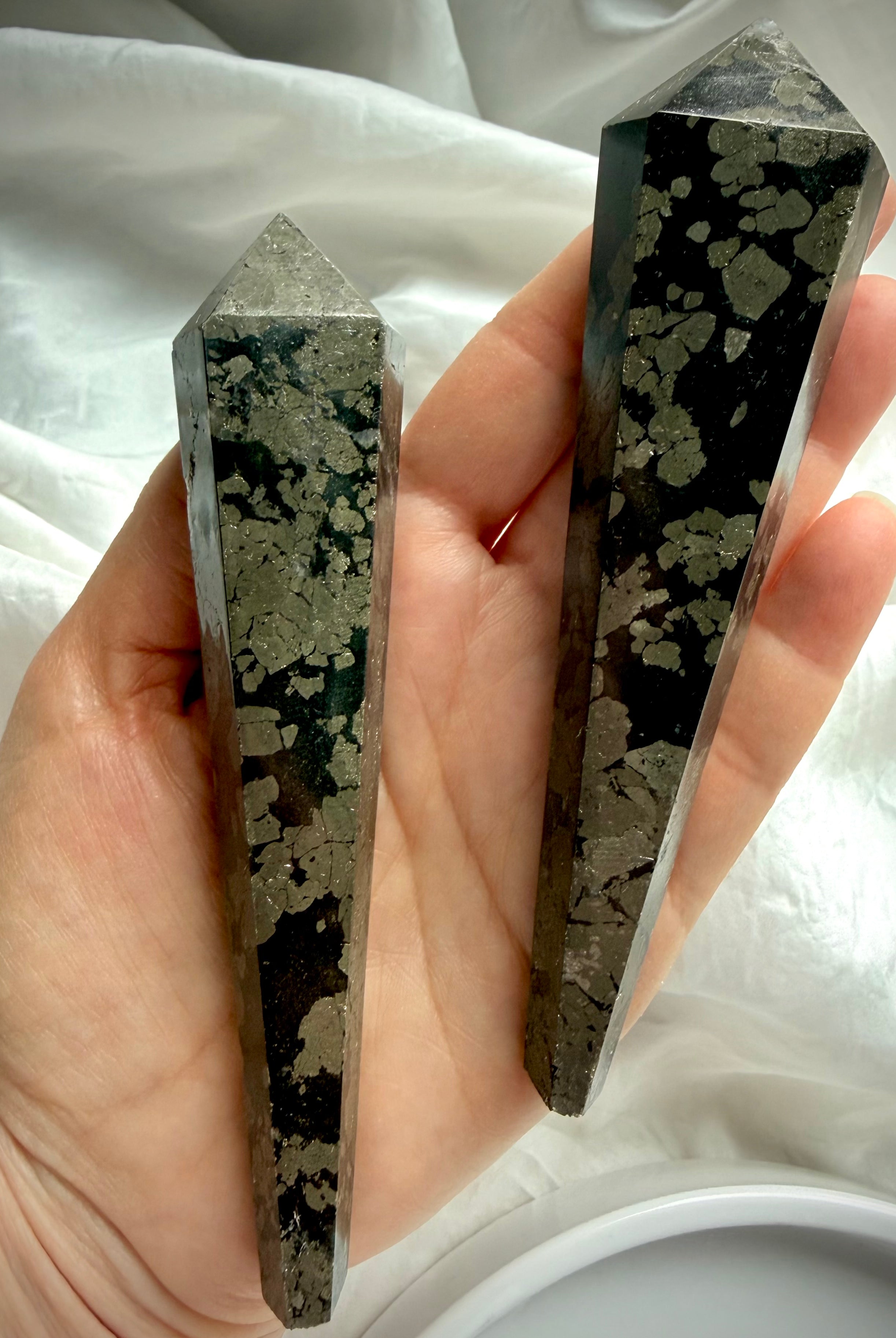 two pyrite wands in black matrix held in hand showing polished crystal points and natural gold pattern
