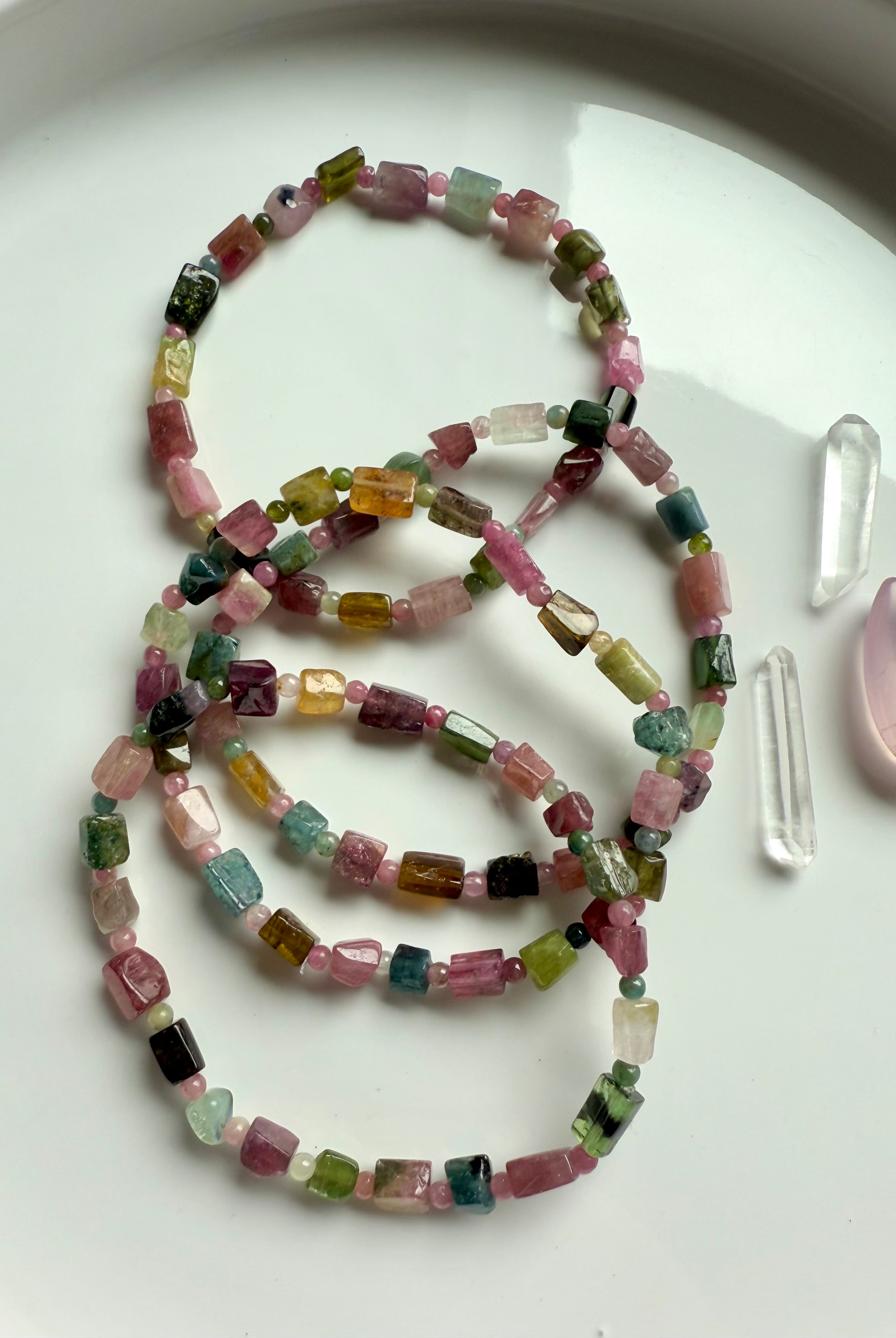 An array of Rainbow Tourmaline Bracelets made with irregular cube shaped gems shown on a white plate