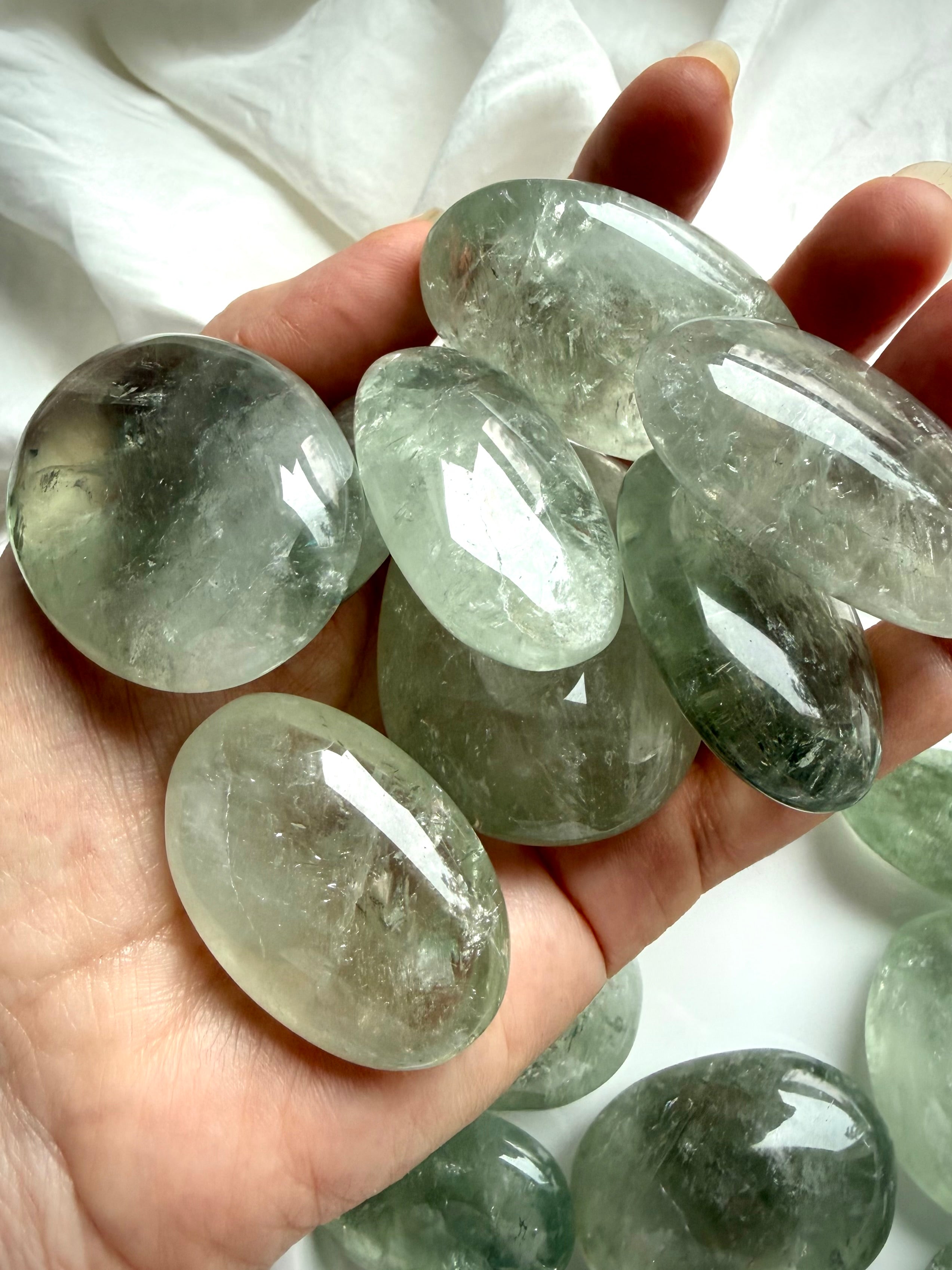 Hand holding polished Prasiolite palm stones in assorted sizes with green translucence