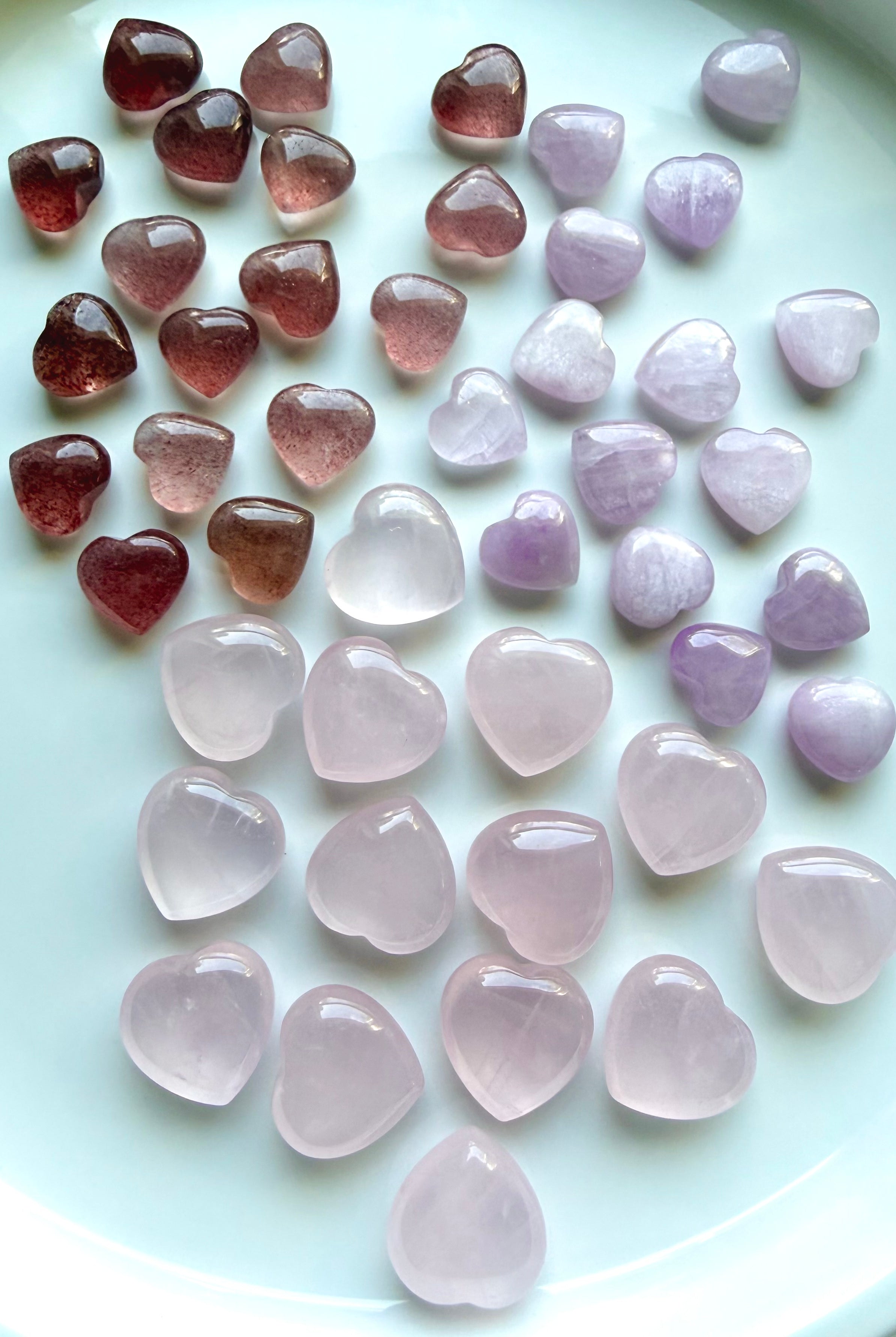Mini rose quartz, strawberry quartz, and kunzite crystal hearts arranged together to show size, shape, and color differences