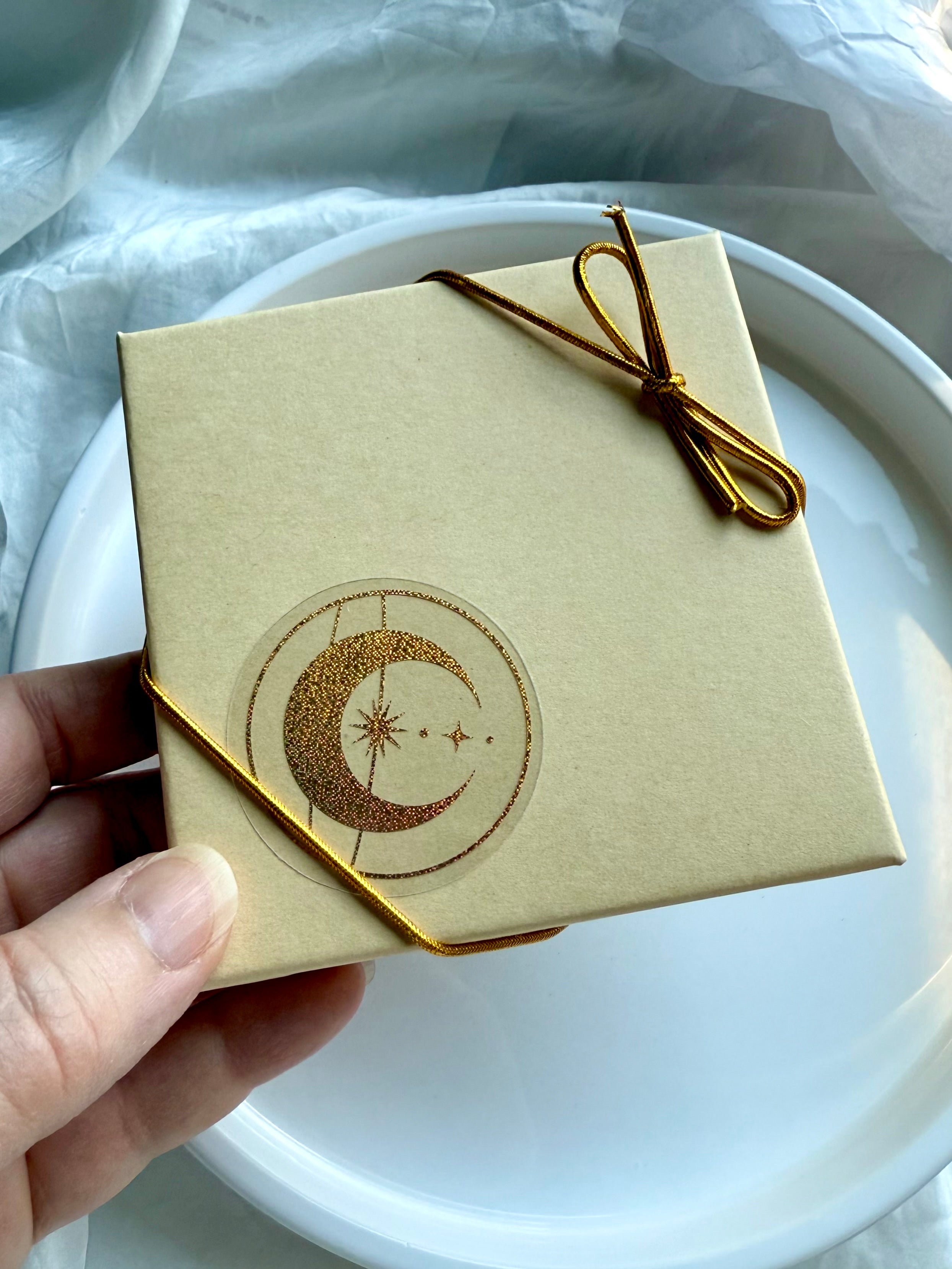 Gift box for Crystal Gifts tied with golden bow and celestial moon star sticker.