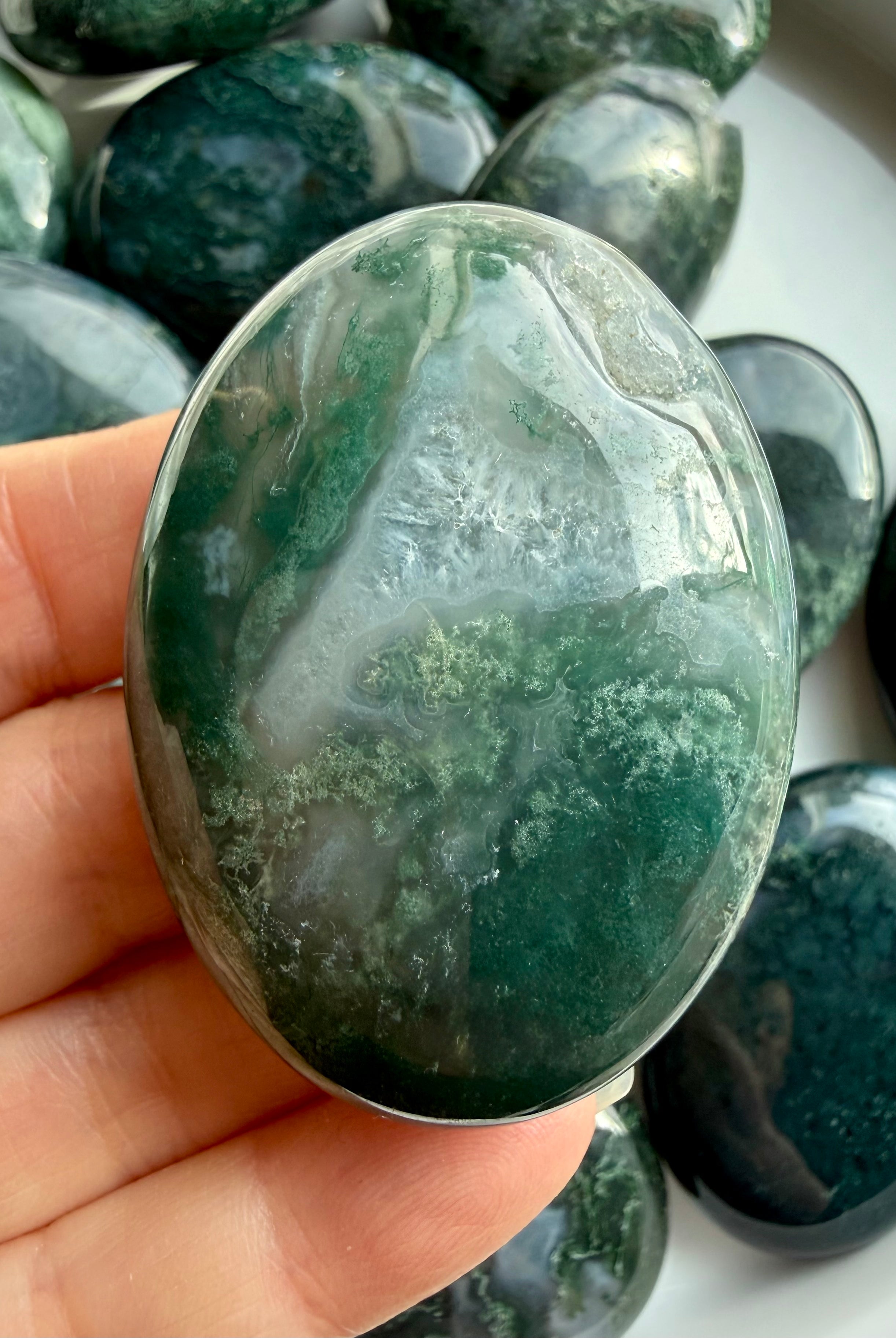 Hand holding moss agate palm stone showing natural dendritic patterns, soothing crystal for nervous system support