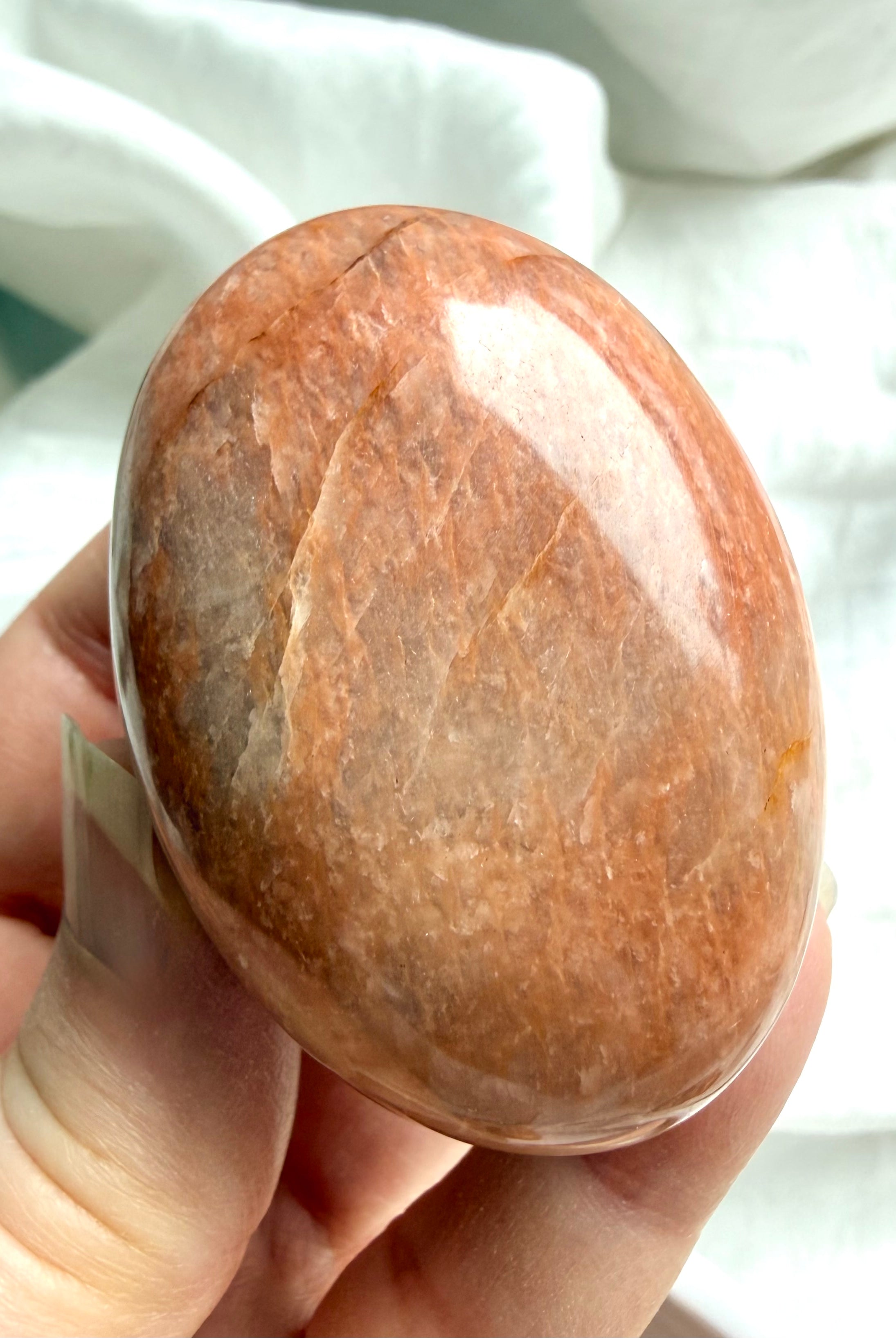 Large Peach Moonstone palm stone held in hand showing natural crack lines and warm orange peach hues