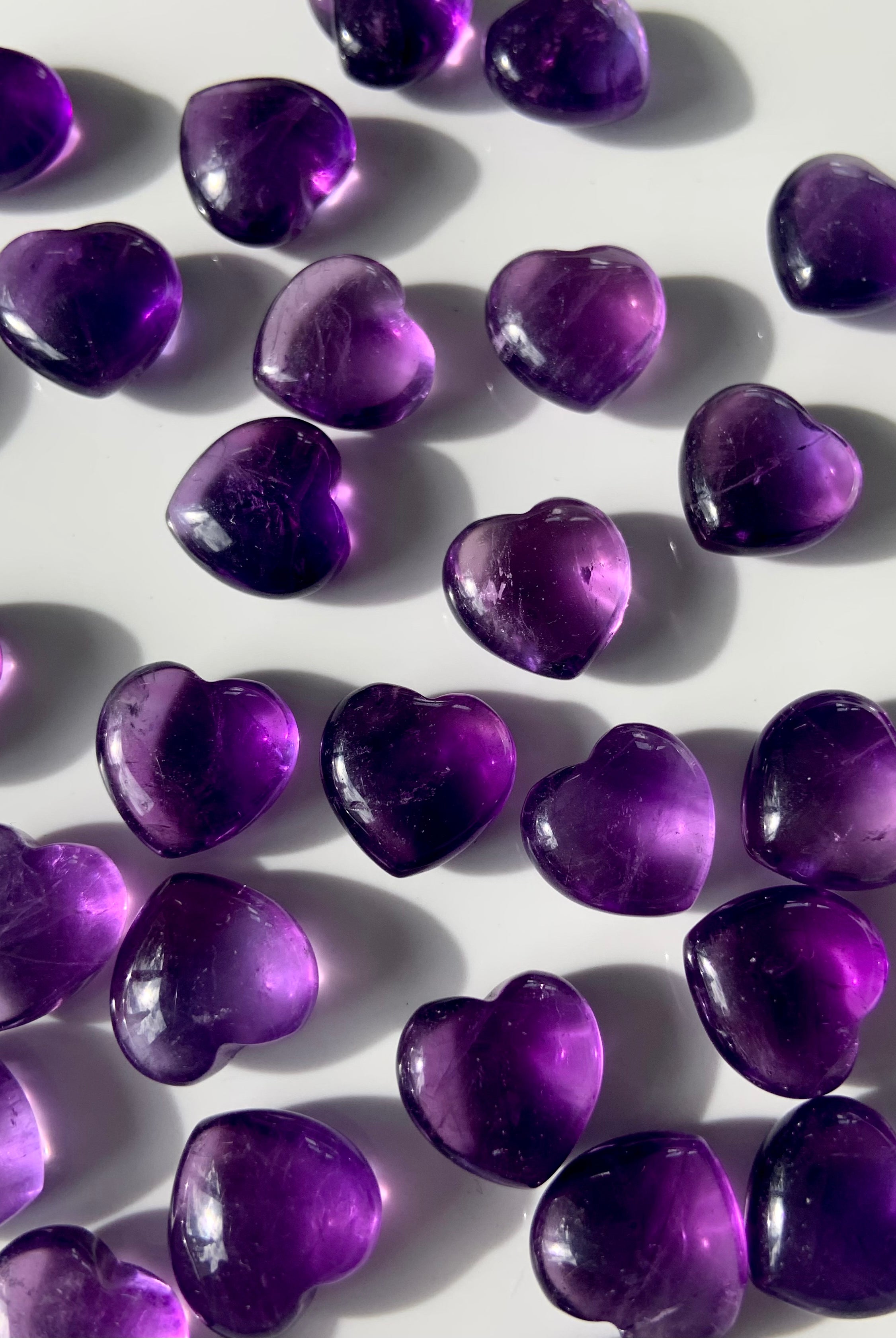 Array of gemmy purple Amethyst hearts on a white background — mini crystals for crown chakra healing