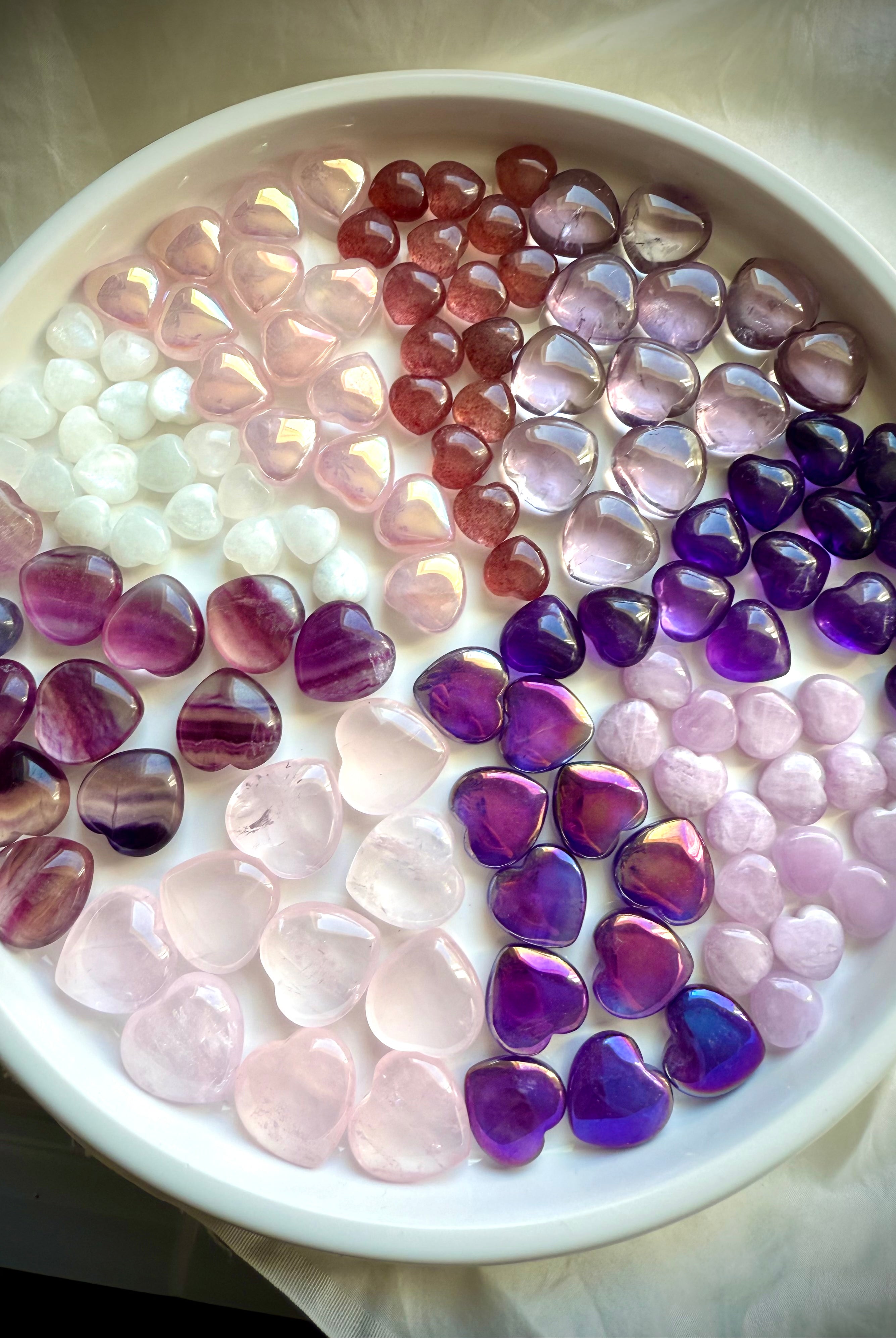 Wide view of multiple pink and purple mini crystal hearts arranged in pie-slice formation by stone type.