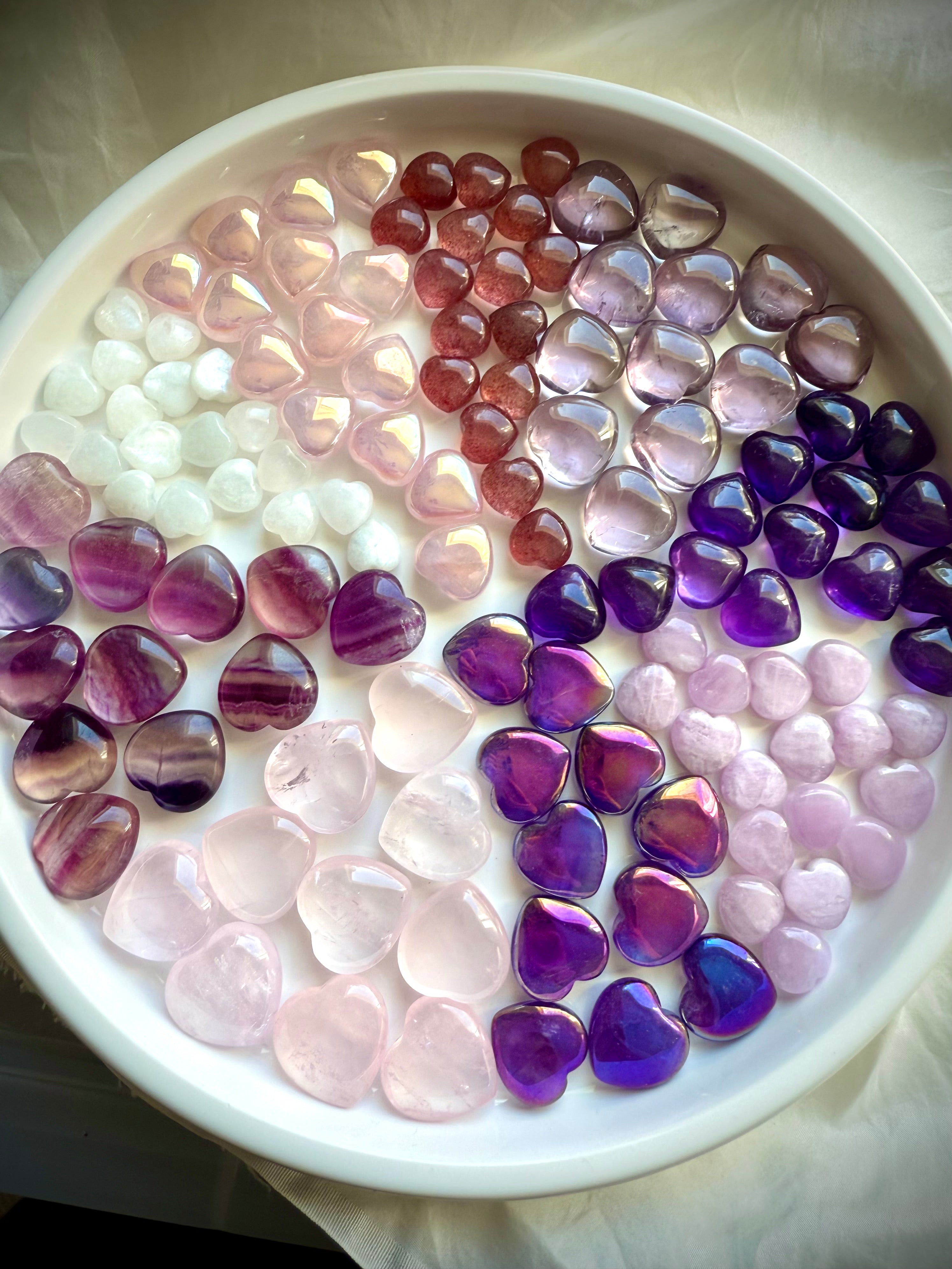 Wide view of multiple pink and purple mini crystal hearts arranged in pie-slice formation by stone type.
