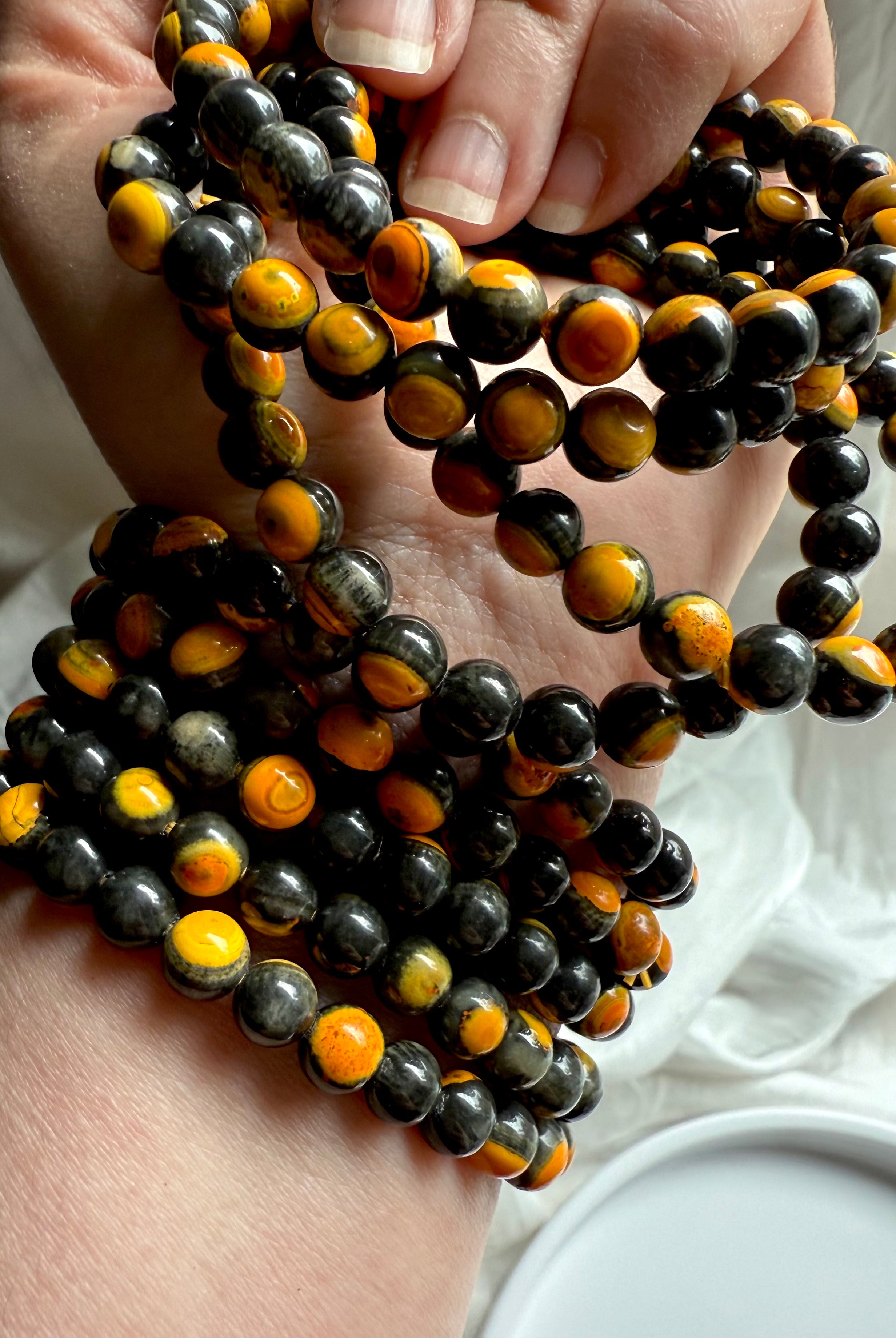 Hand holding several vibrant bumblebee jasper bracelets, vivid yellow-orange stone with earthy black inclusions for vitality and inner strength