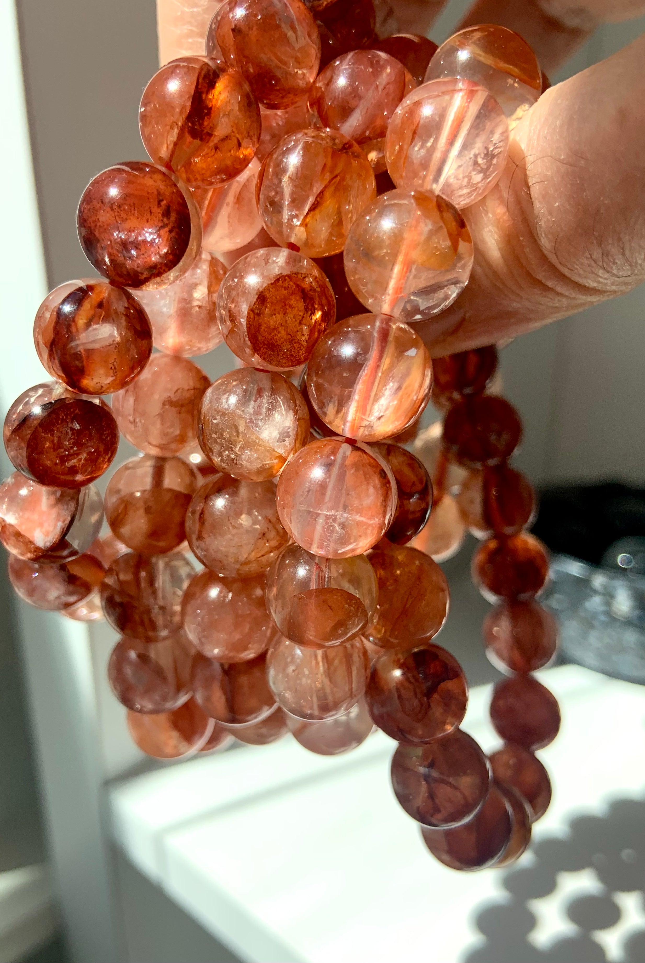 Stack of Fire Quartz bracelets held to the light, highlighting the translucent beads and fiery inclusions of Hematoid Quartz
