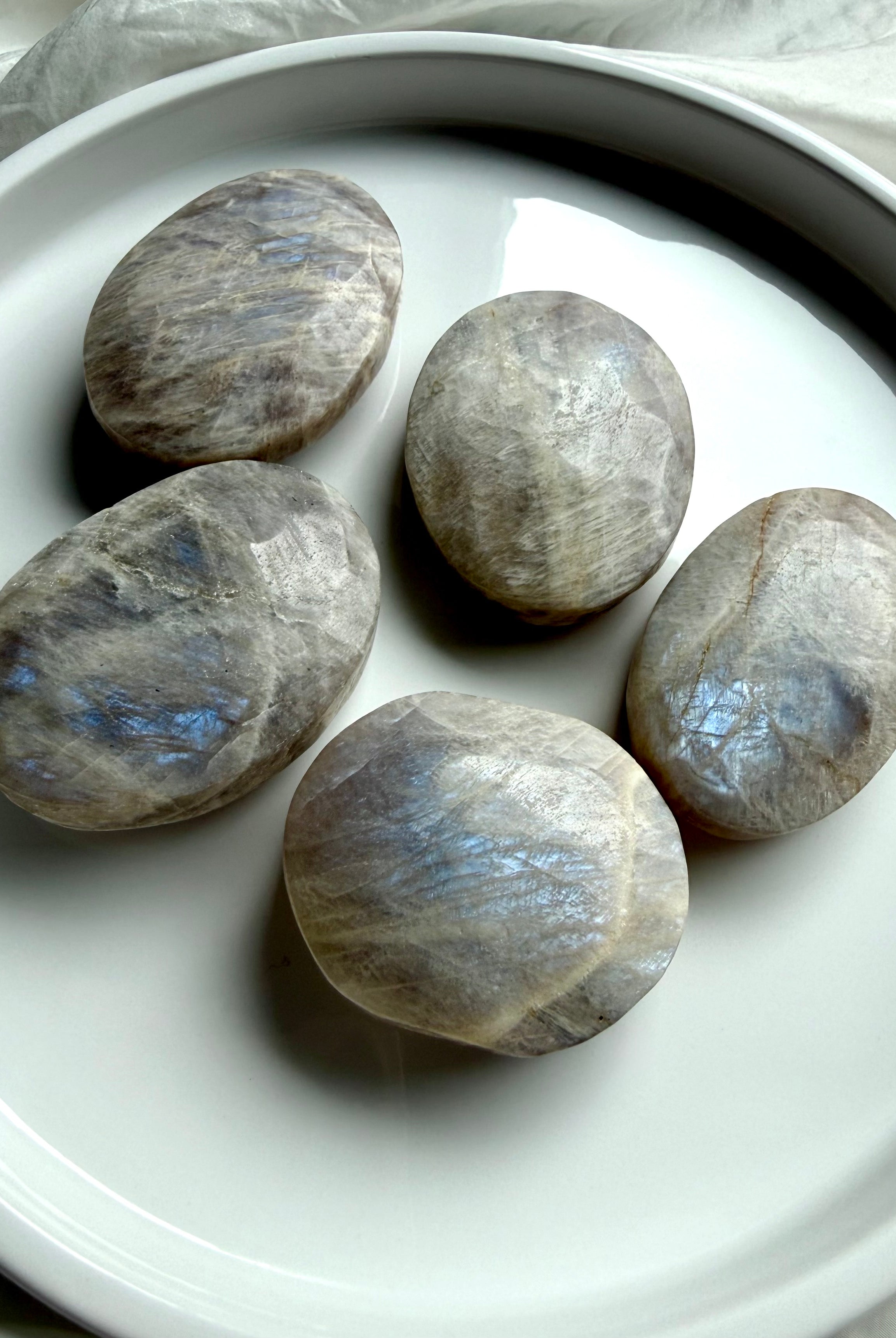 belomorite moonstone palm stones with blue flash and silvery shimmer on a white ceramic tray
