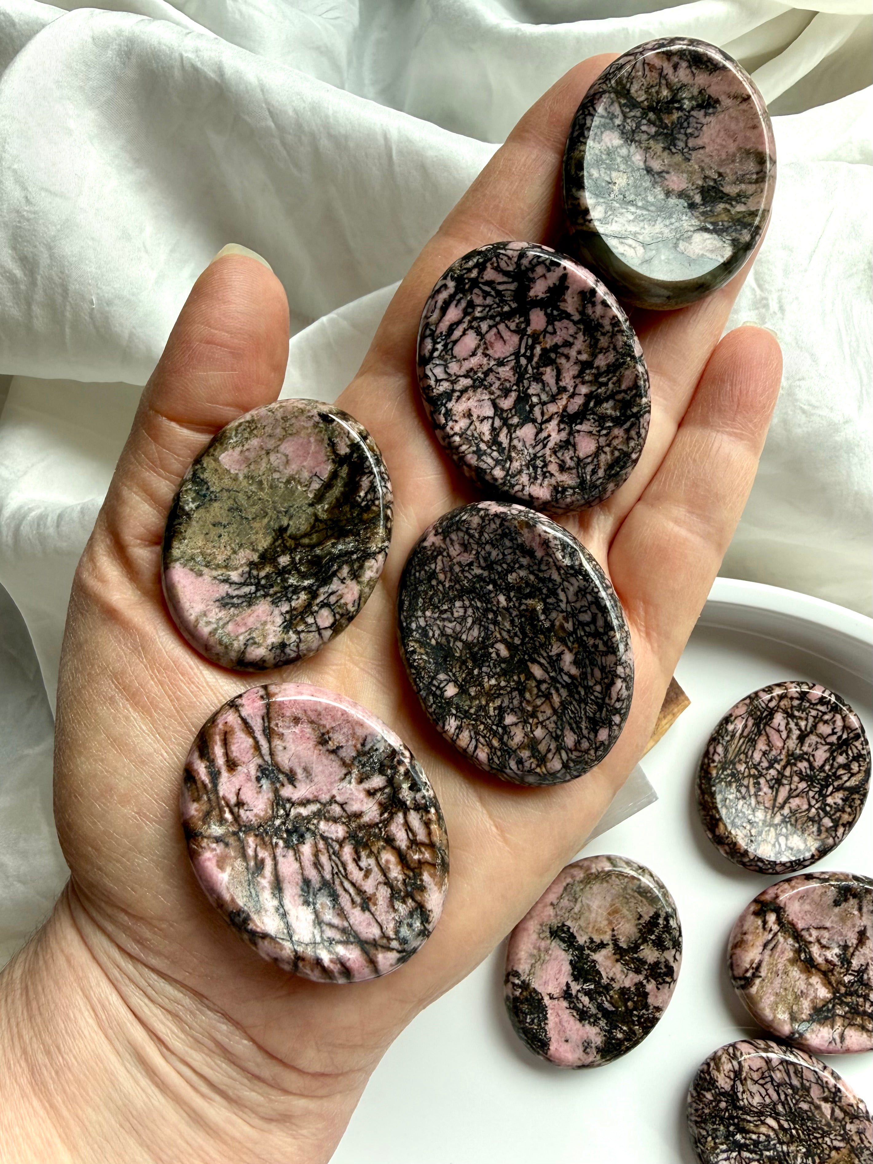 Rhodonite worry stones in hand showing pink and black spiderweb matrix patterns