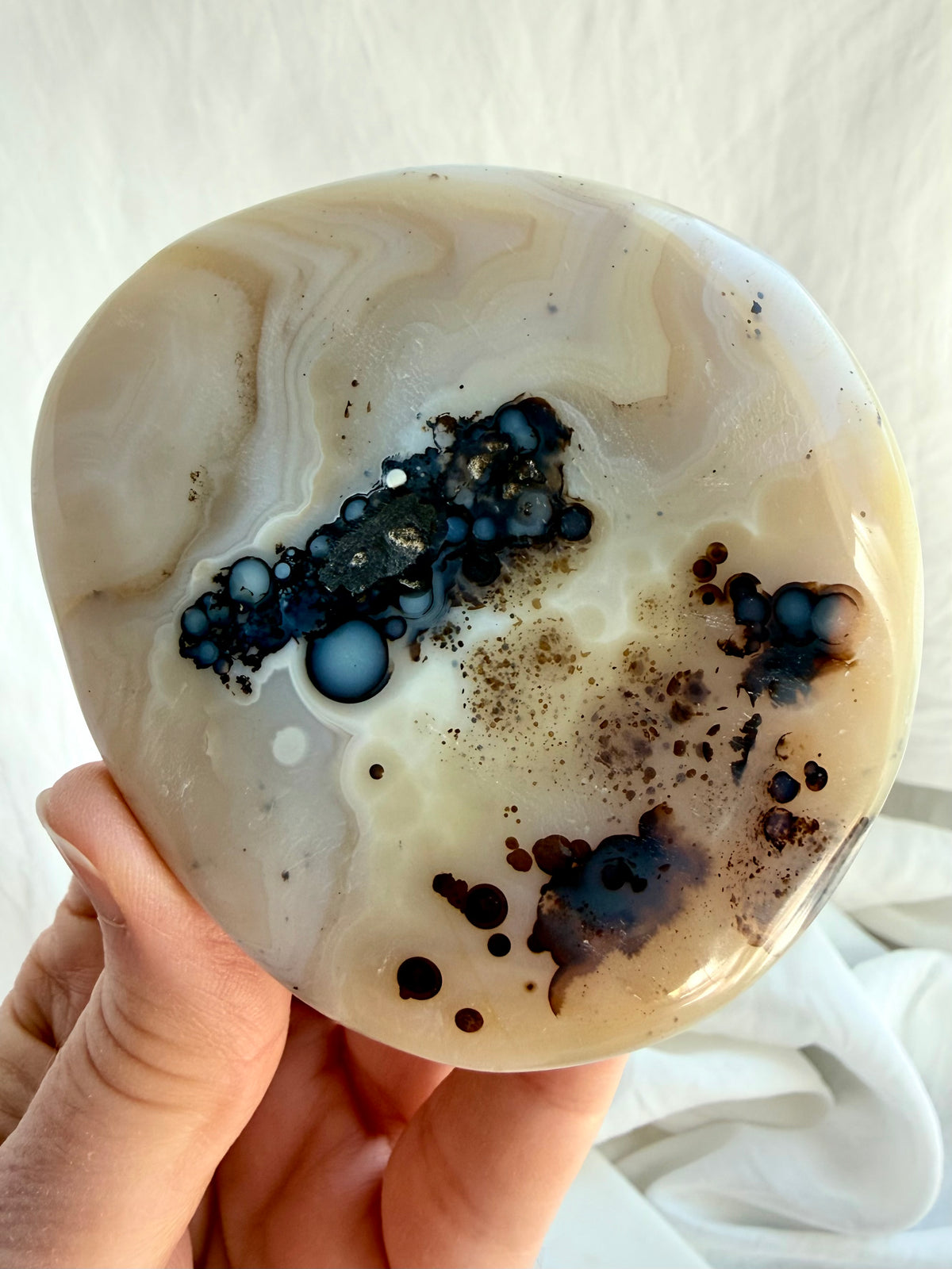 Dendritic Agate healing crystal held in hand, featuring dramatic black inclusions and soft ivory tones for grounding and growth