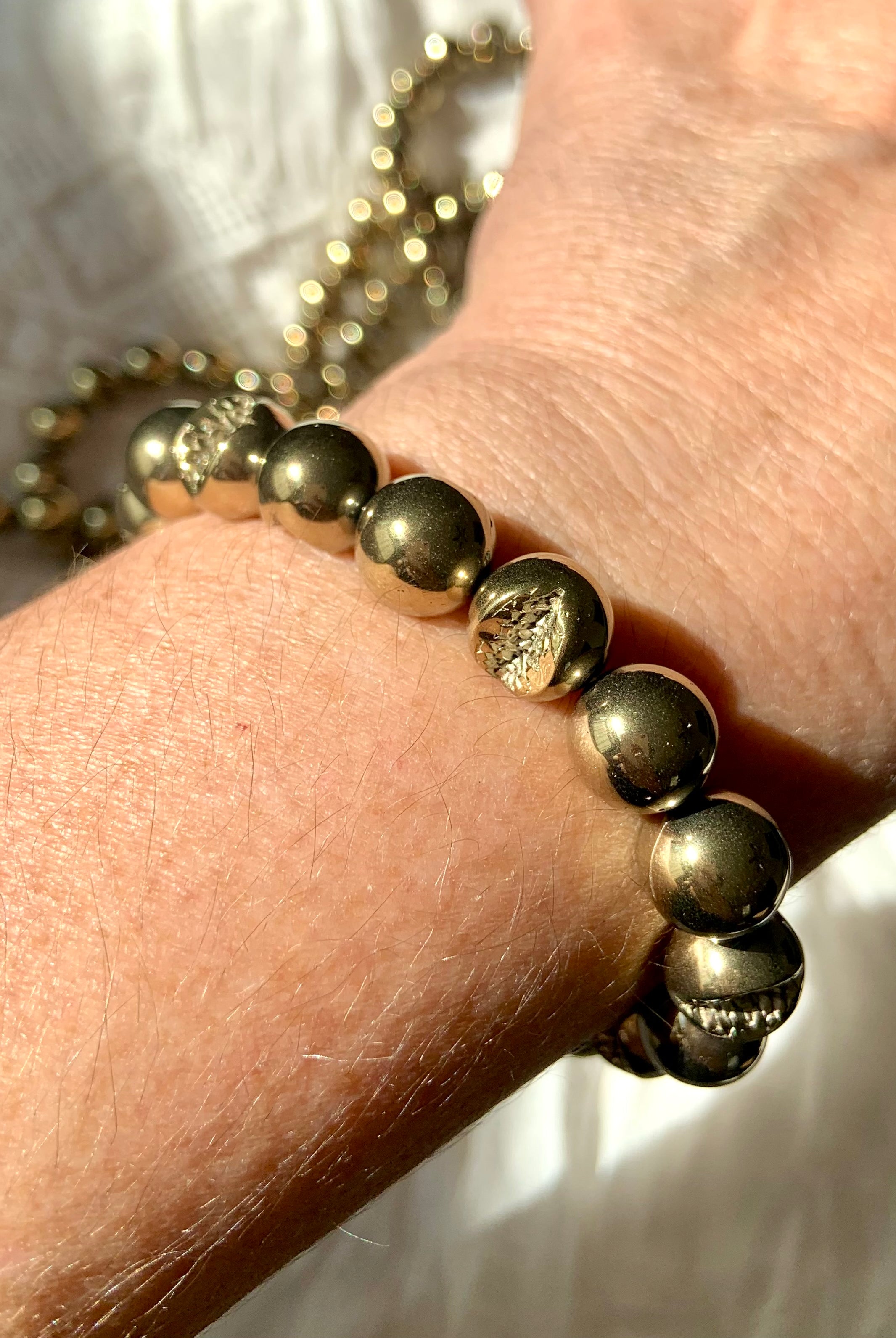 Pyrite beaded bracelet worn on wrist, reflecting light with metallic golden tones — healing crystal jewelry for strength & empowerment.