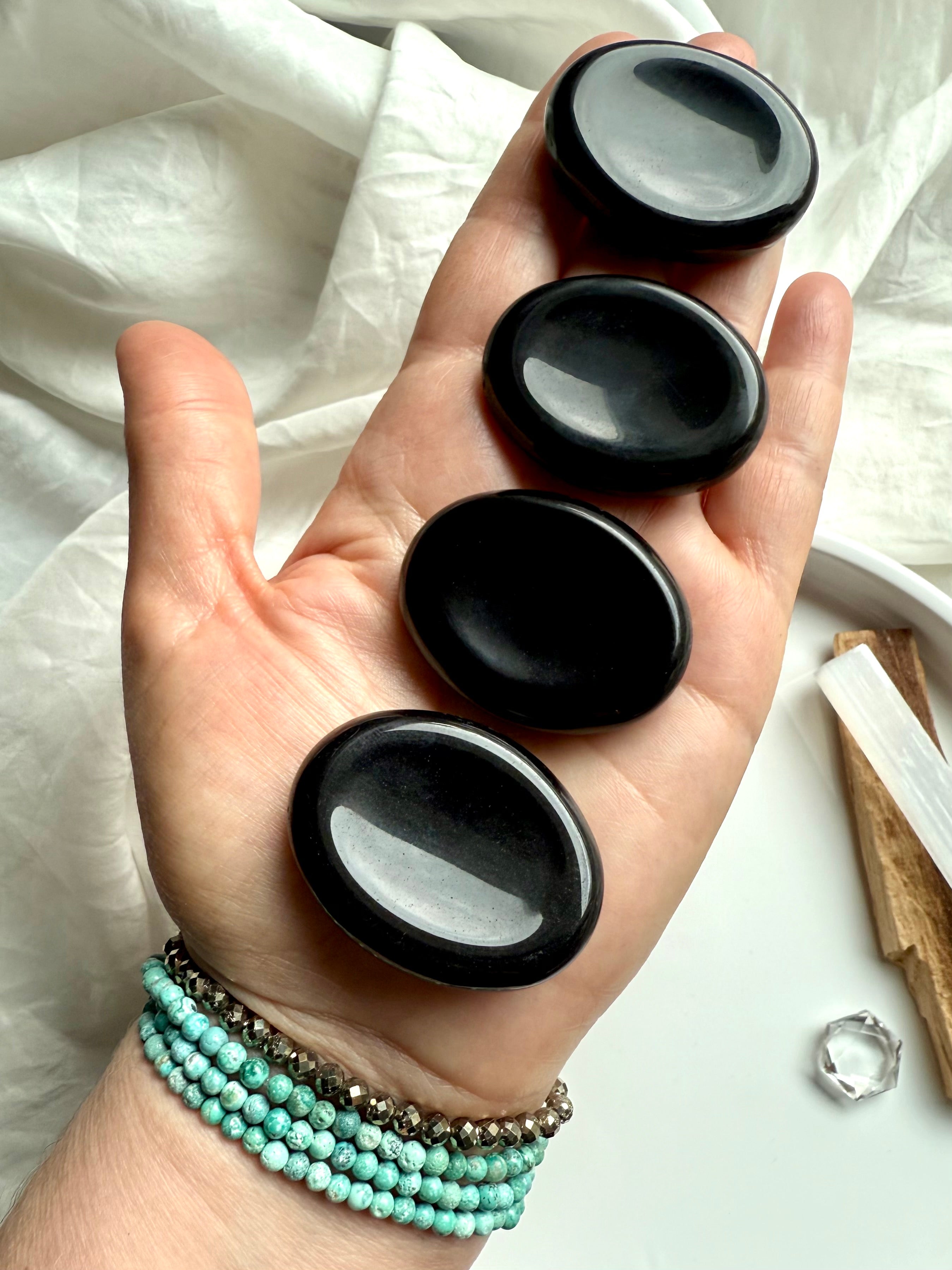 Black Obsidian palm stones lined up in hand – root chakra crystals for grounding, calming + daily energy clearing