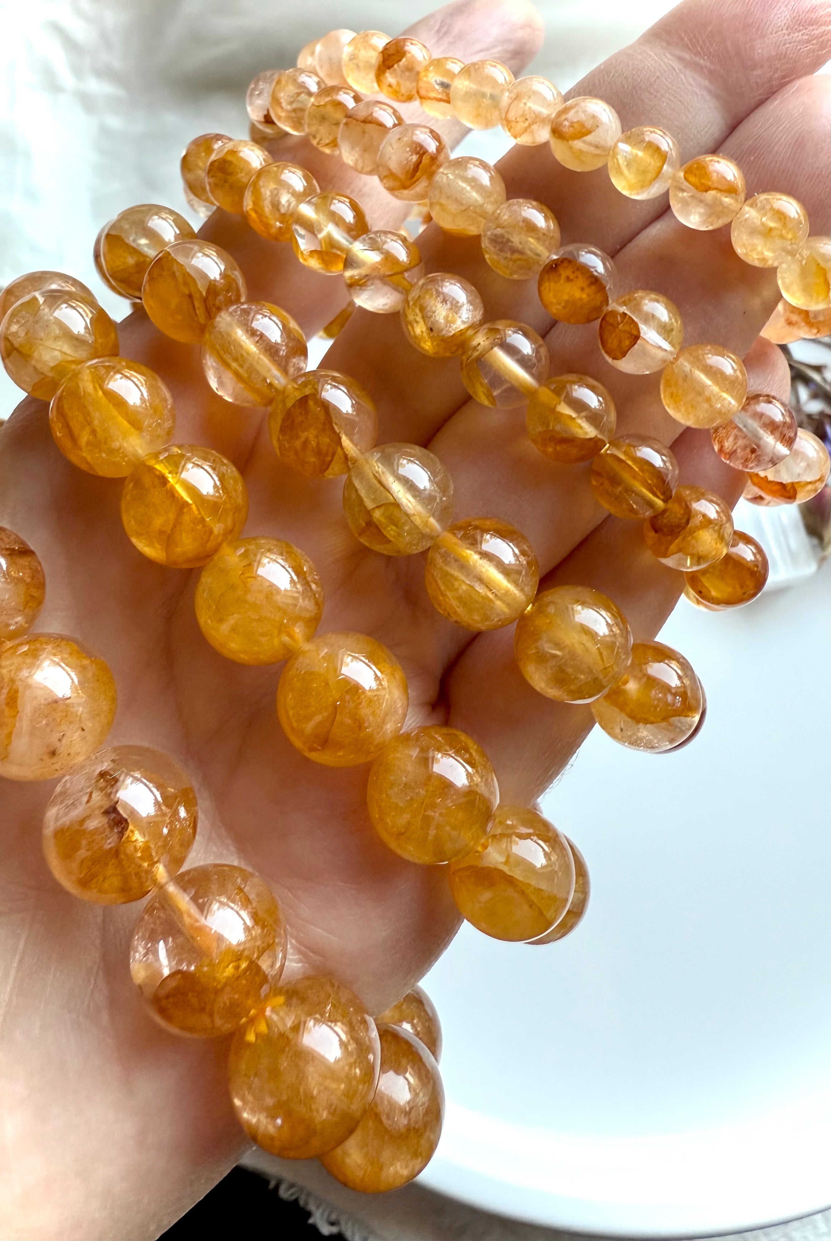 Angled view of stacked Golden Healer Quartz bracelets in bead sizes large to small, displayed on hand to highlight radiant color and inclusions.