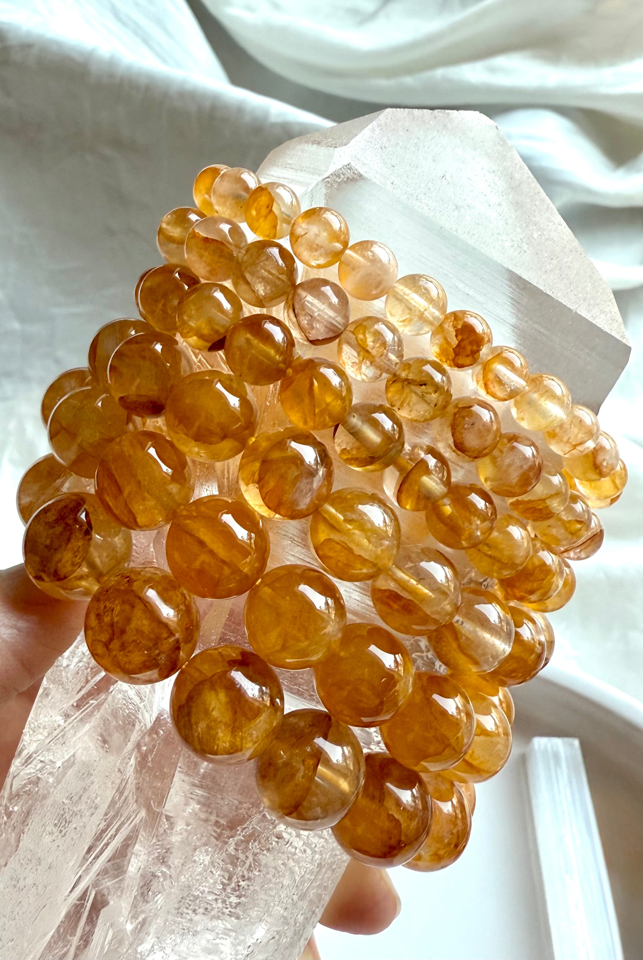 Stack of six high quality Golden Healer Quartz bracelets displayed on a large quartz point, showing bead sizes from large to small with luminous golden color and clarity.