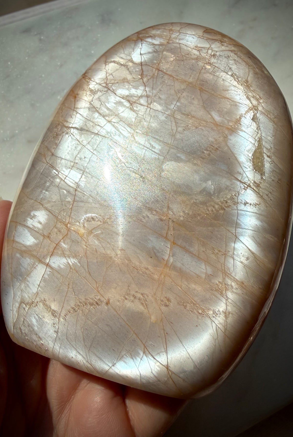Peach Moonstone crystal freeform held in hand showing bright silver flash across the polished surface