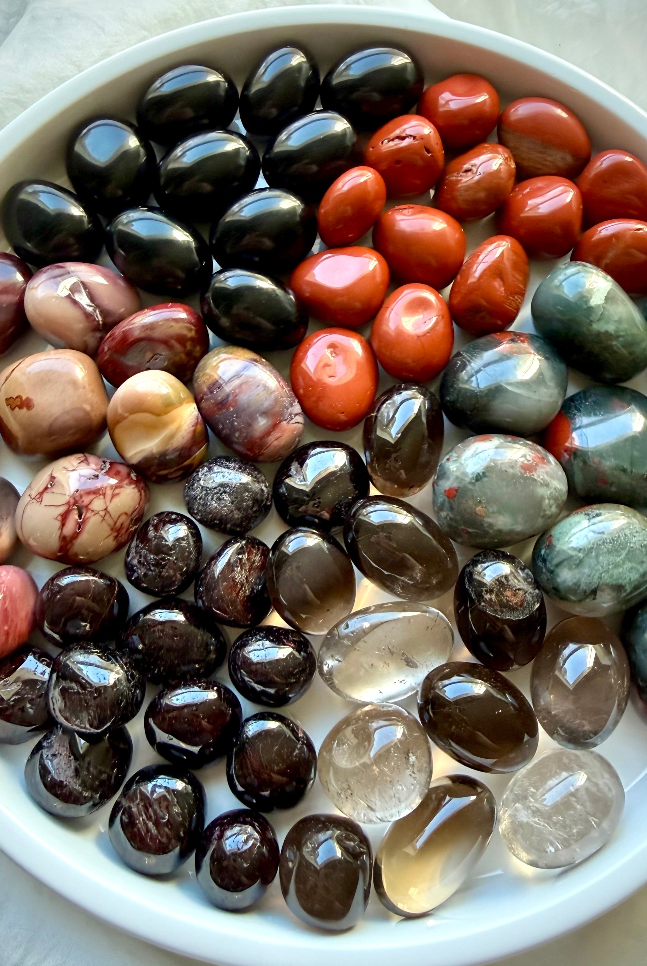 Root Chakra healing stones arranged in a white bowl with Bloodstone, Black Obsidian, Red Jasper, Smoky Quartz, and Garnet