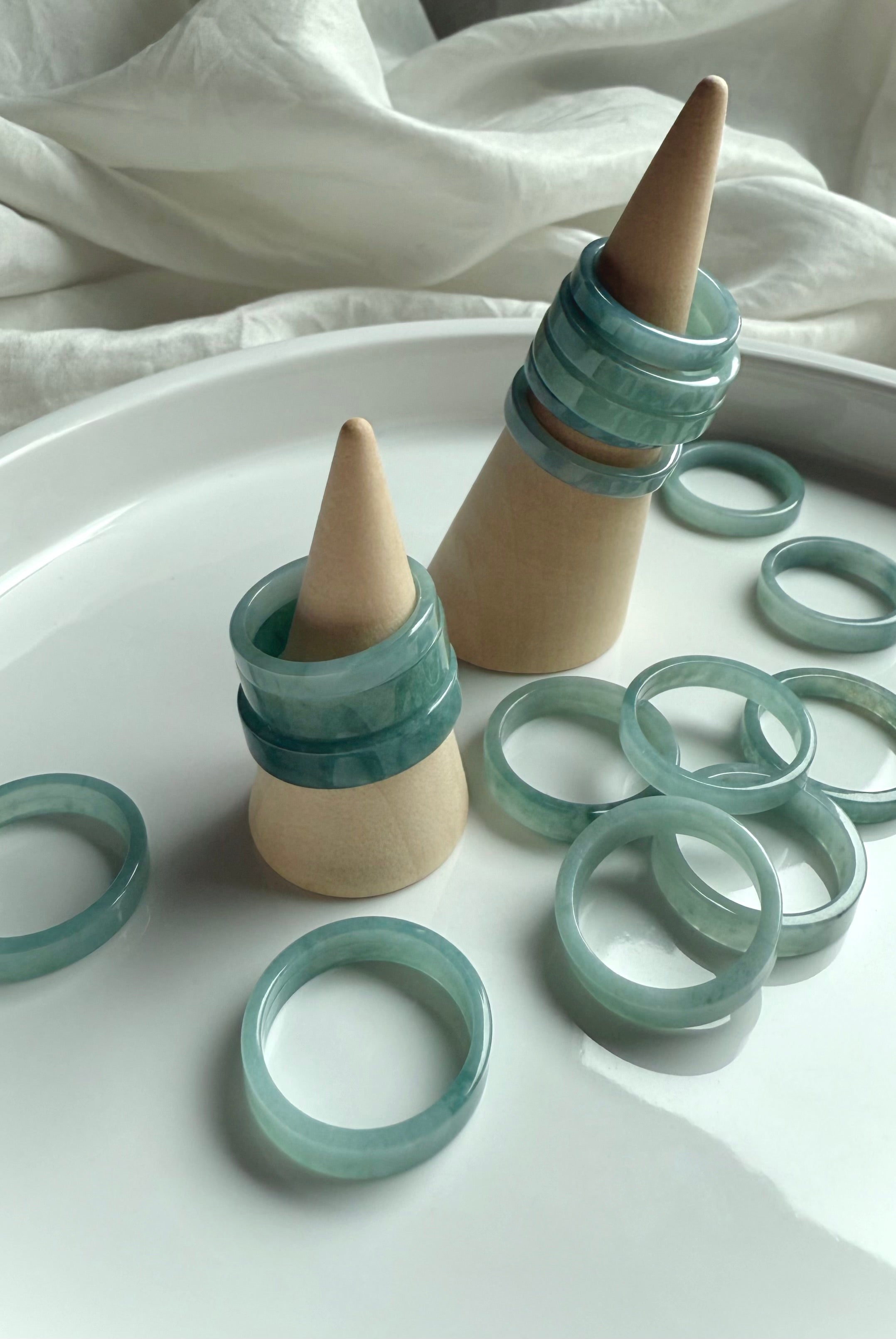 Natural Blue Water Jade rings stacked on wooden ring cones, showcasing flat jadeite bands in calming aqua-green tones for heart chakra healing and crystal jewelry gifting