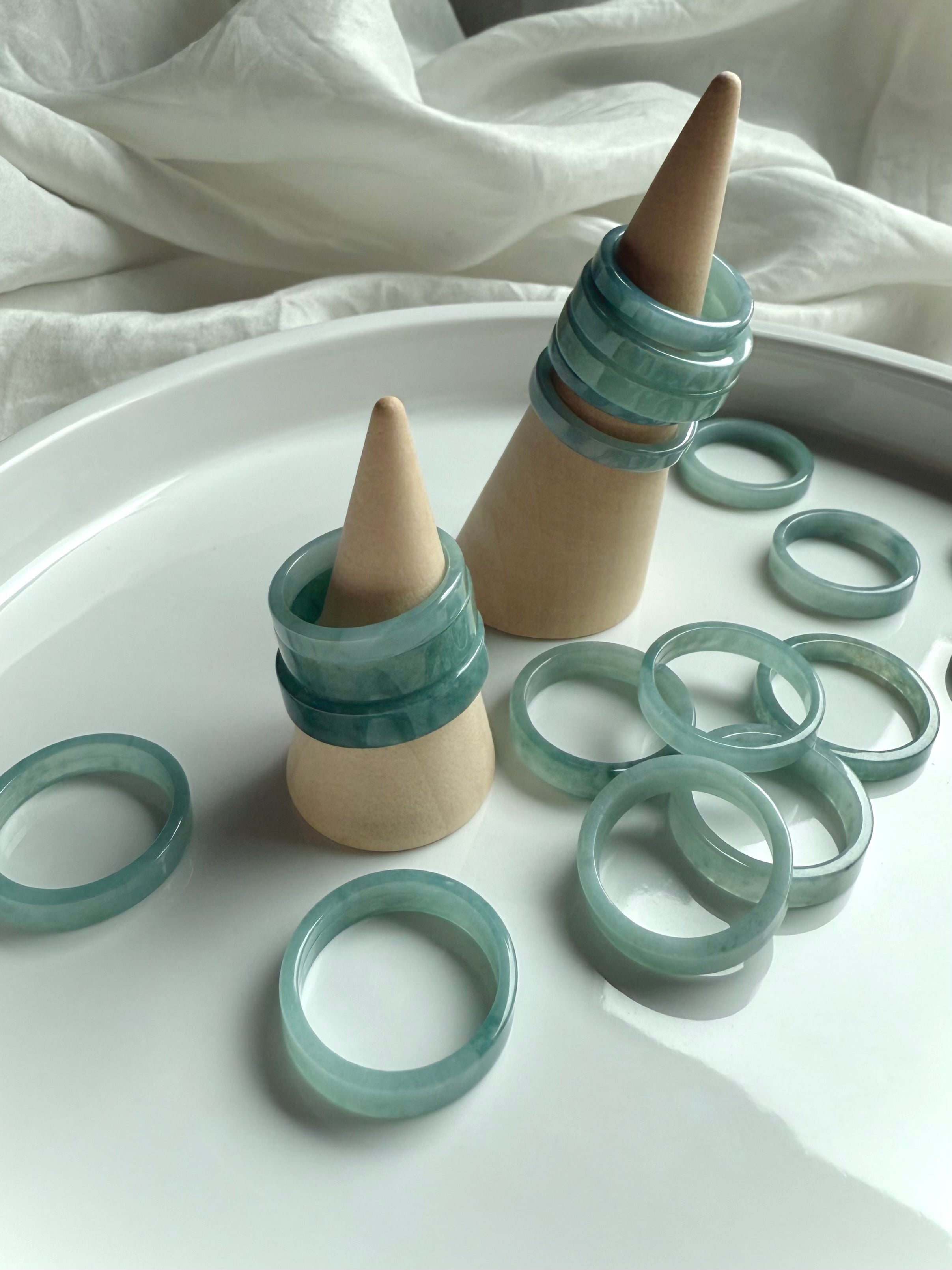 Natural Blue Water Jade rings stacked on wooden ring cones, showcasing flat jadeite bands in calming aqua-green tones for heart chakra healing and crystal jewelry gifting