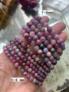 Green Unicorn Stone bracelets โ Watermelon Tourmaline in Lepidolite โ held over mirror in 5โ6mm and 7โ8mm bead sizes. Healing crystal jewelry for stress relief + grounding