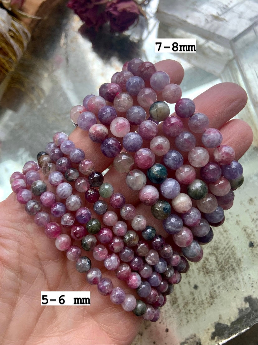 Green Unicorn Stone bracelets โ Watermelon Tourmaline in Lepidolite โ held over mirror in 5โ6mm and 7โ8mm bead sizes. Healing crystal jewelry for stress relief + grounding
