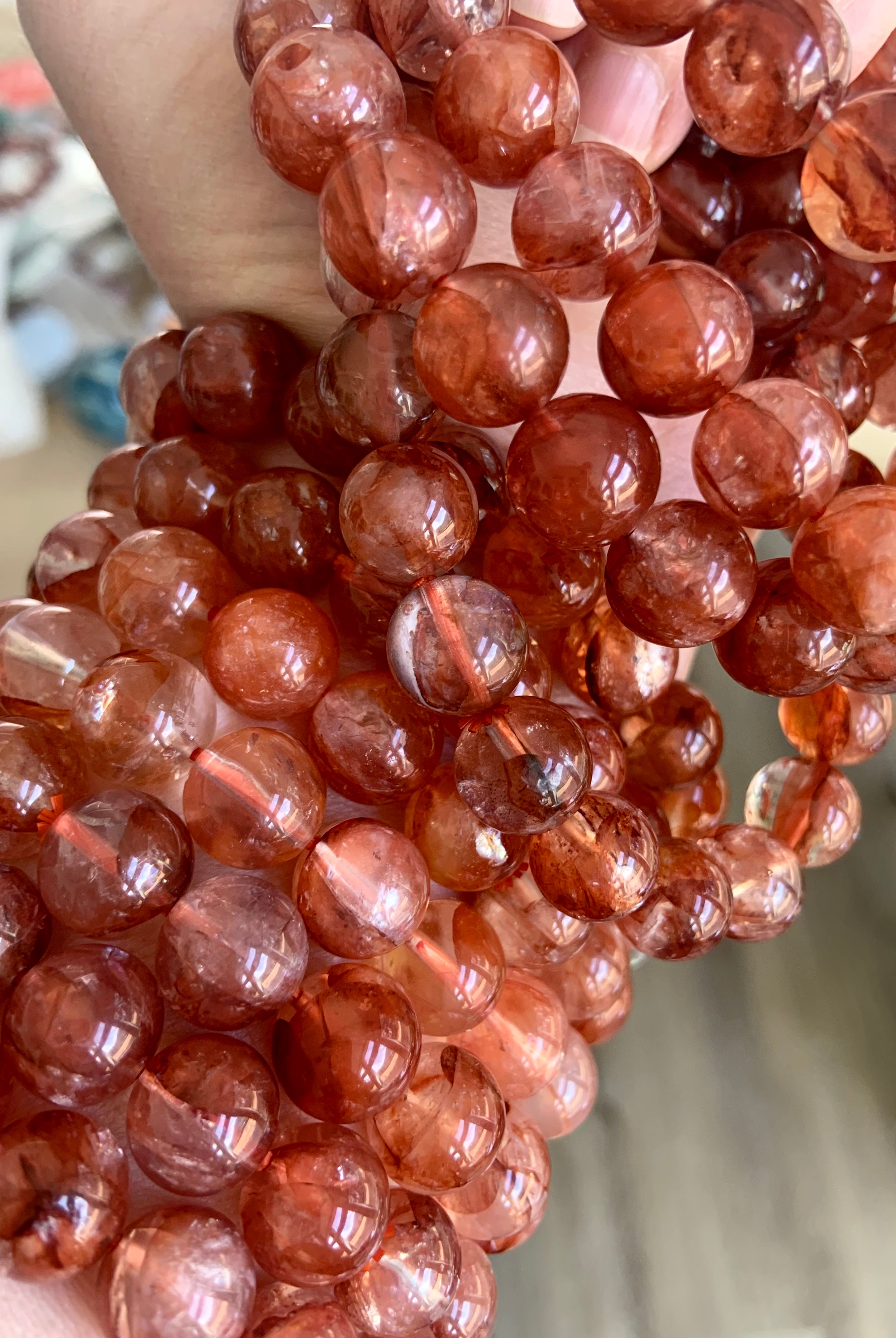 Stack of red Hematoid Quartz bracelets worn on wrist and held in hand, displaying variety and detail in the crystal beads