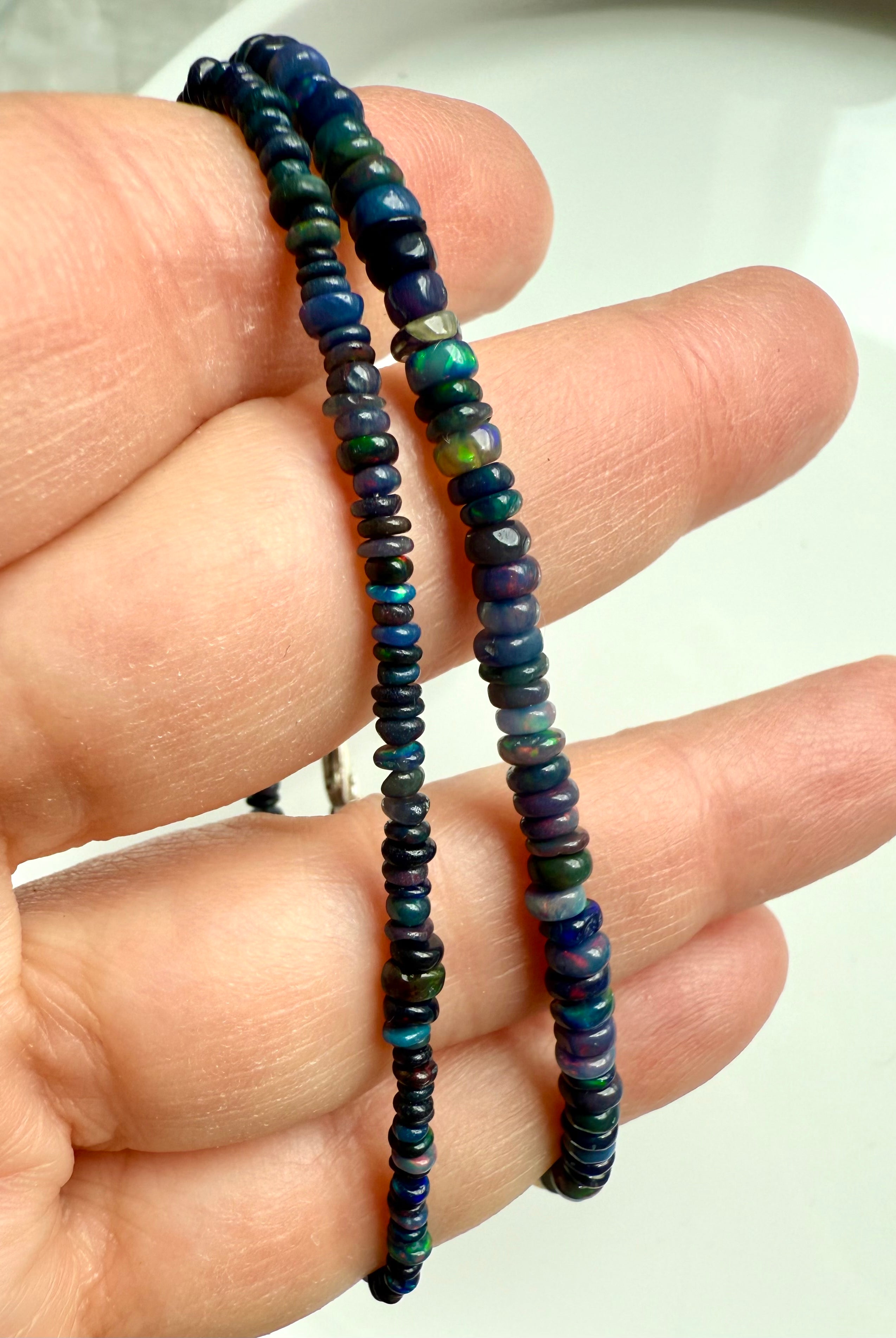 Close-up of two Black Fire Opal bracelets in different bead sizes — luminous Ethiopian opal beads with blue fire and rainbow sheen.