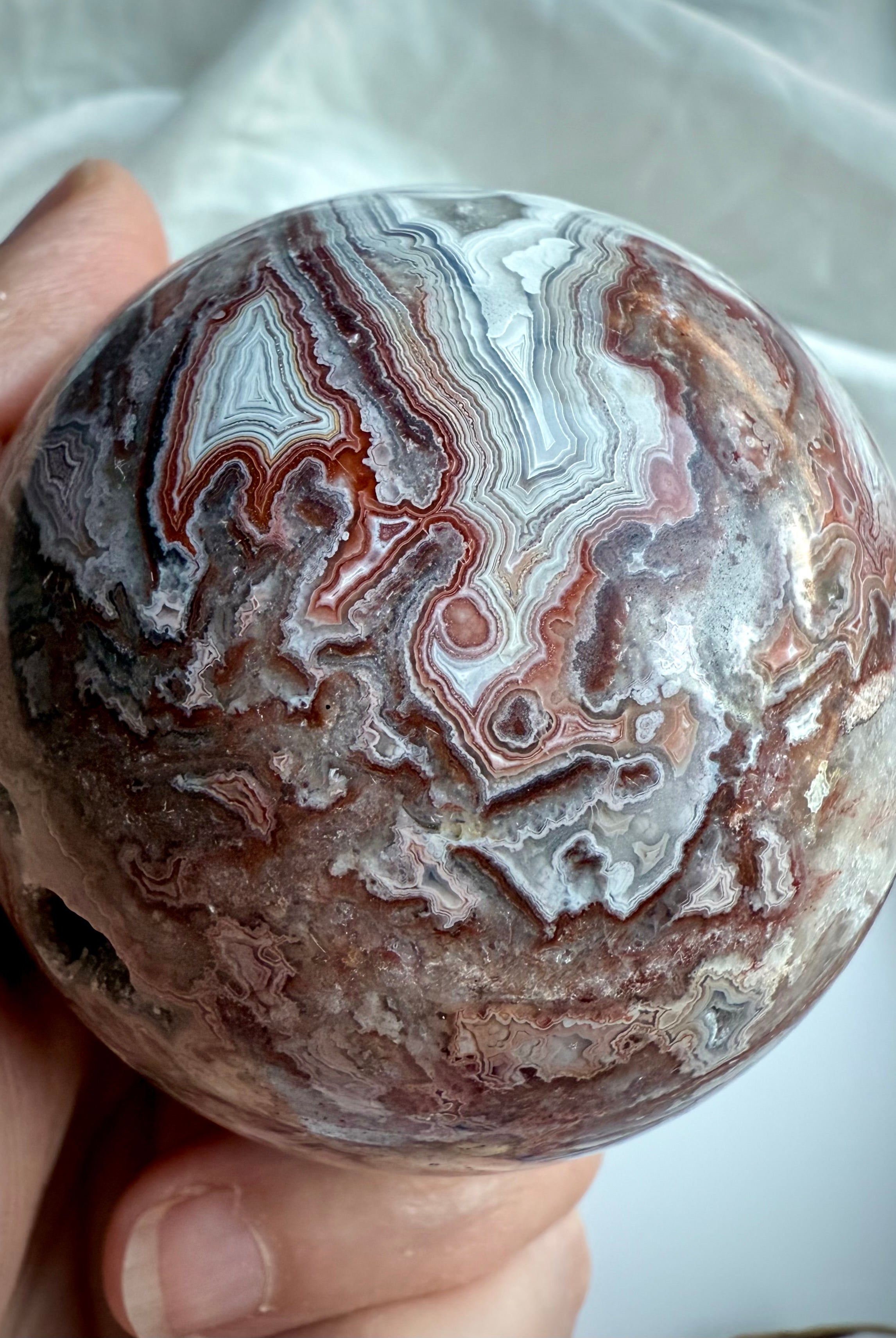 Closeup of Crazy Lace Agate sphere with bold red, white, and gray banding and root chakra